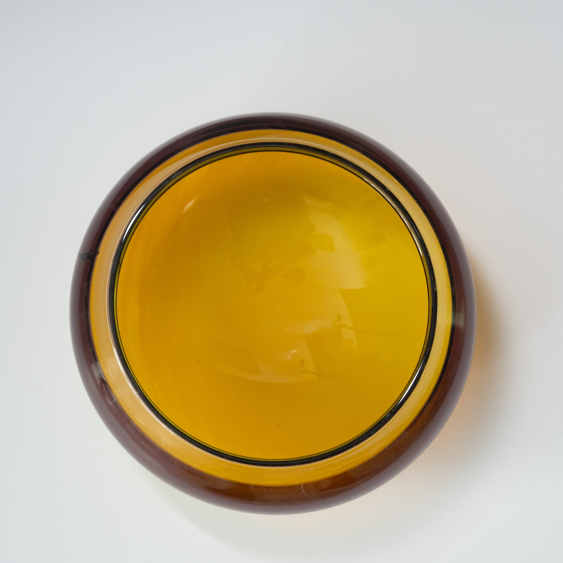Round glass object with yellow center and brown rim on a white background