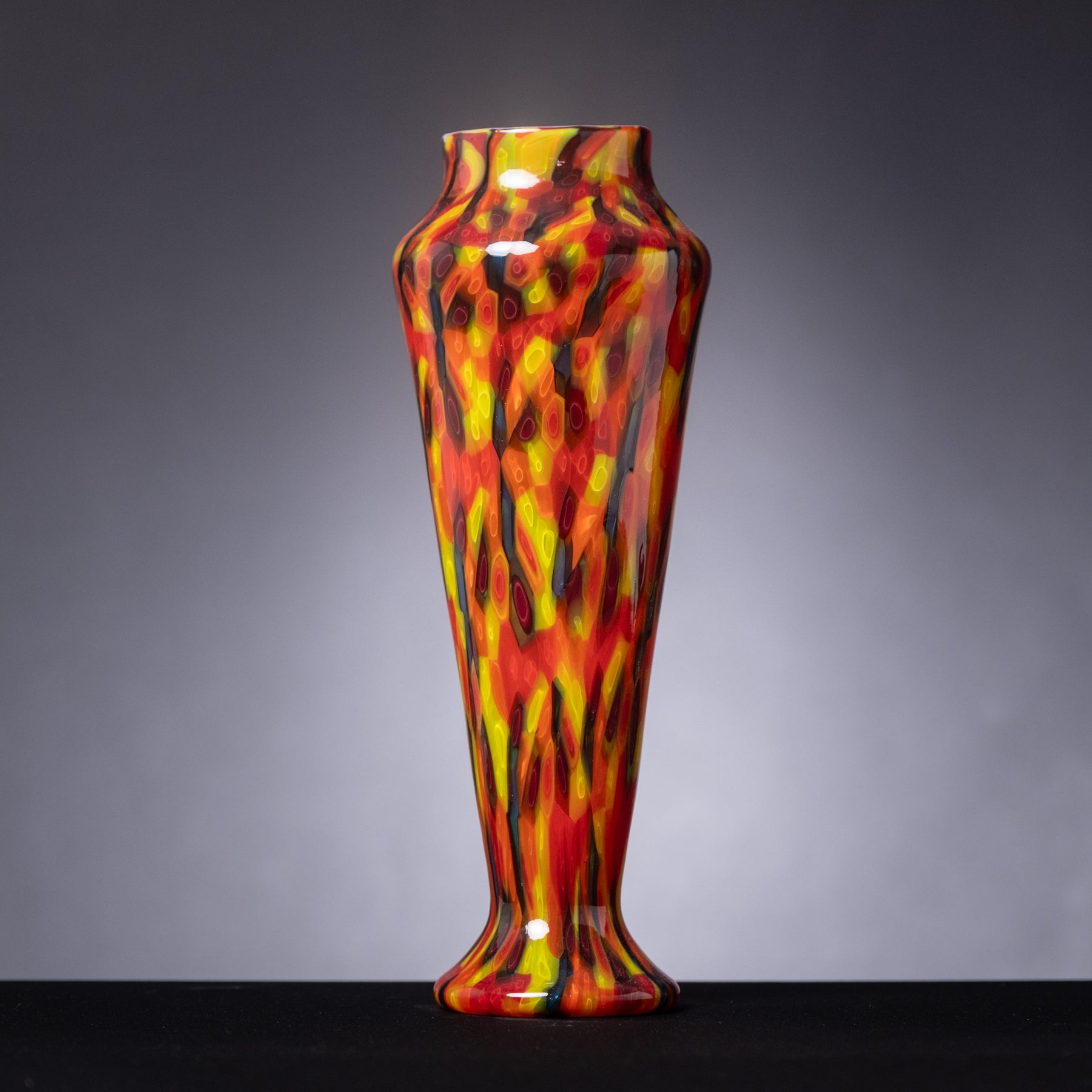Colorful glass vase with flame-like pattern on a gray background
