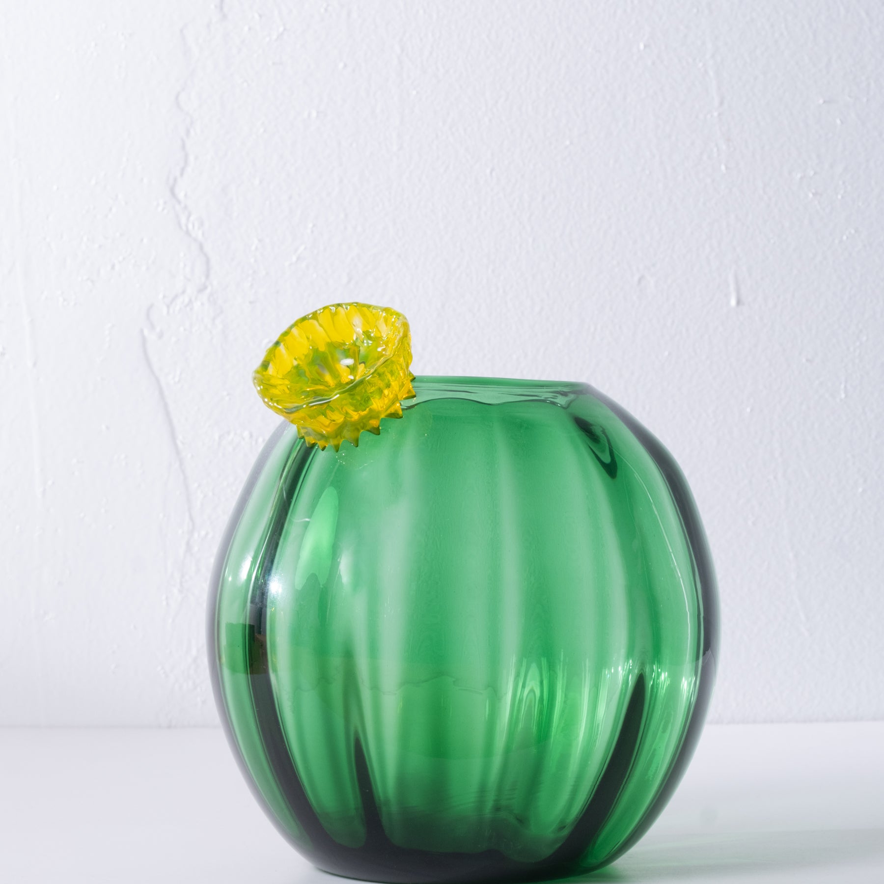 Green glass cactus with yellow flower on white background.