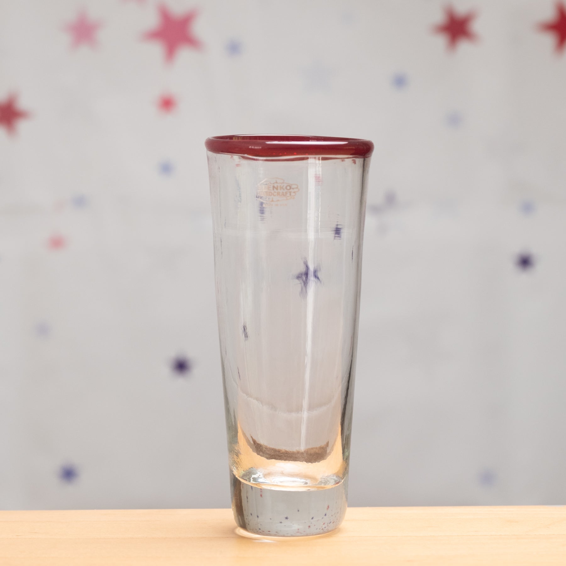 Clear glass with red rim on a wooden surface and star-patterned background