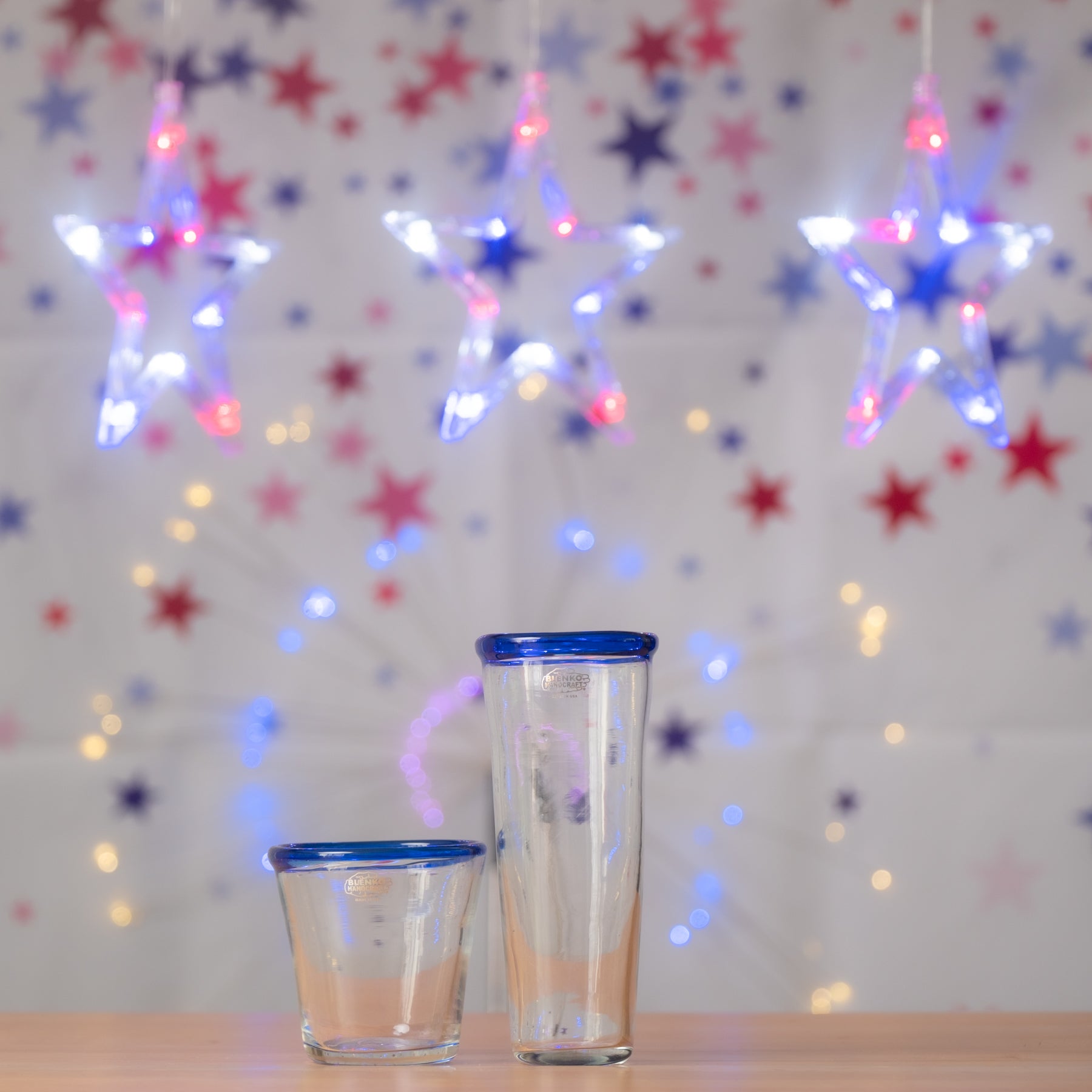 Two glass tumblers with blue rims on a wooden surface with a festive star-patterned background.