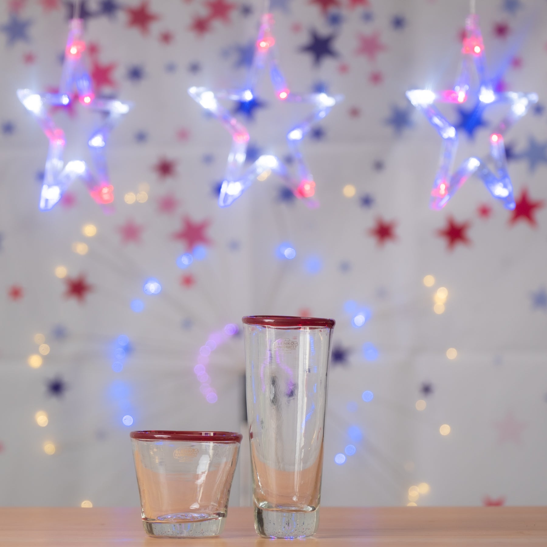 Two glasses with red rims on a table in front of a festive background with colorful lights and stars.
