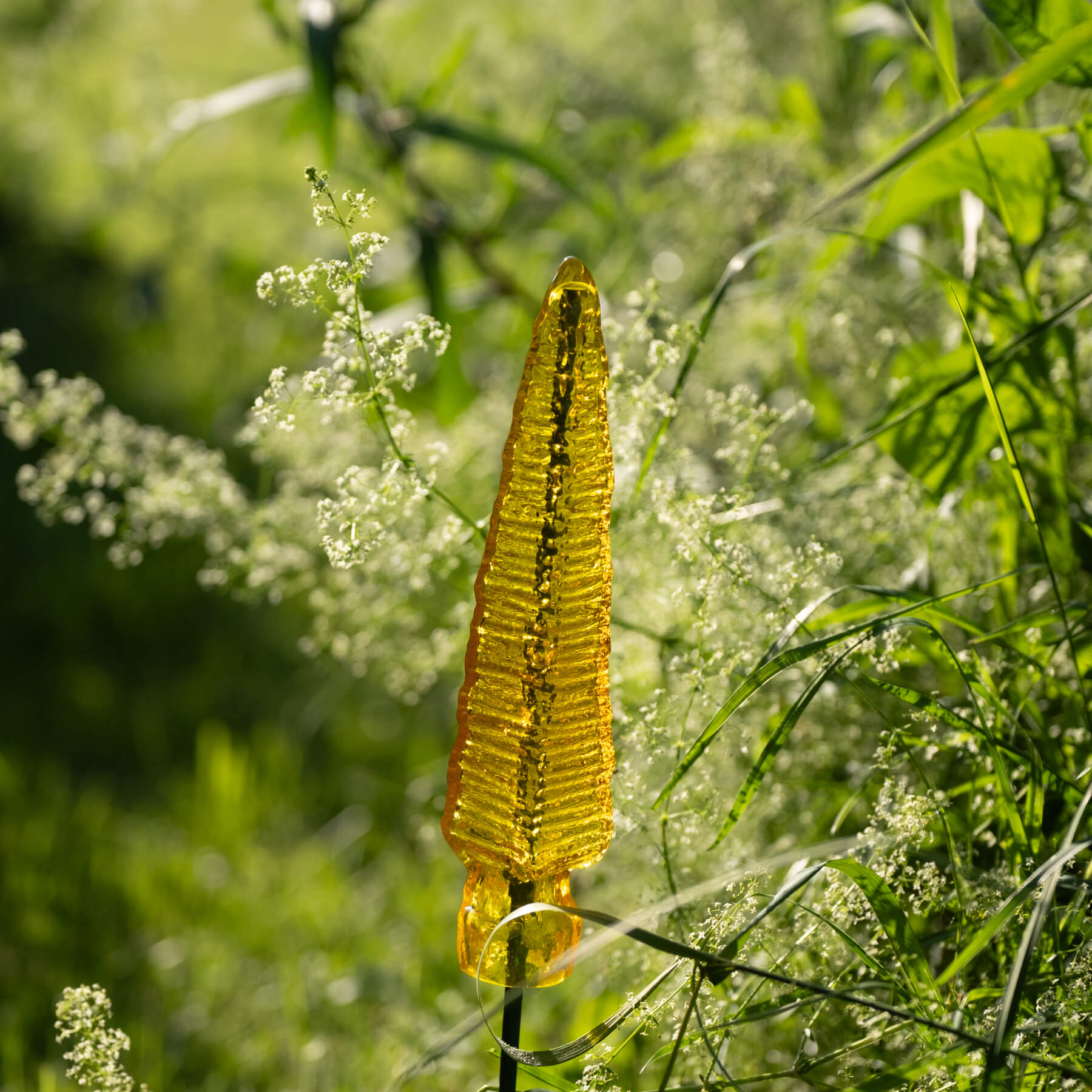 Yellow glass sculpture among green foliage