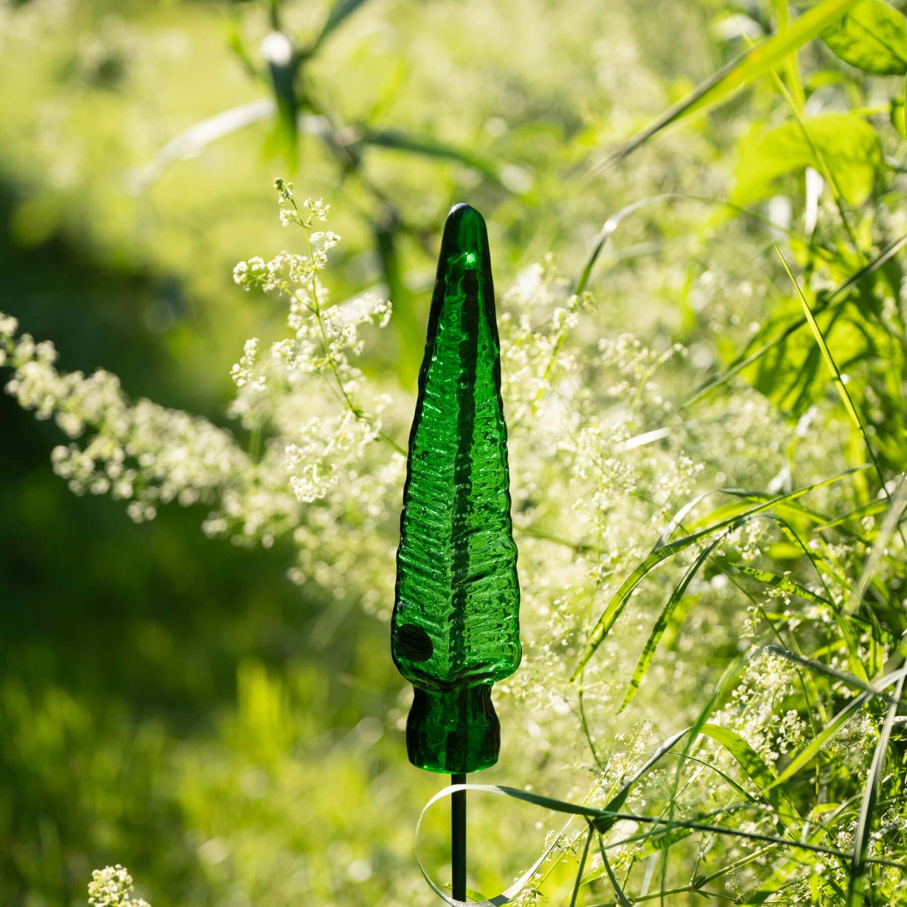 Green glass garden ornament in a natural setting with grass and flowers.