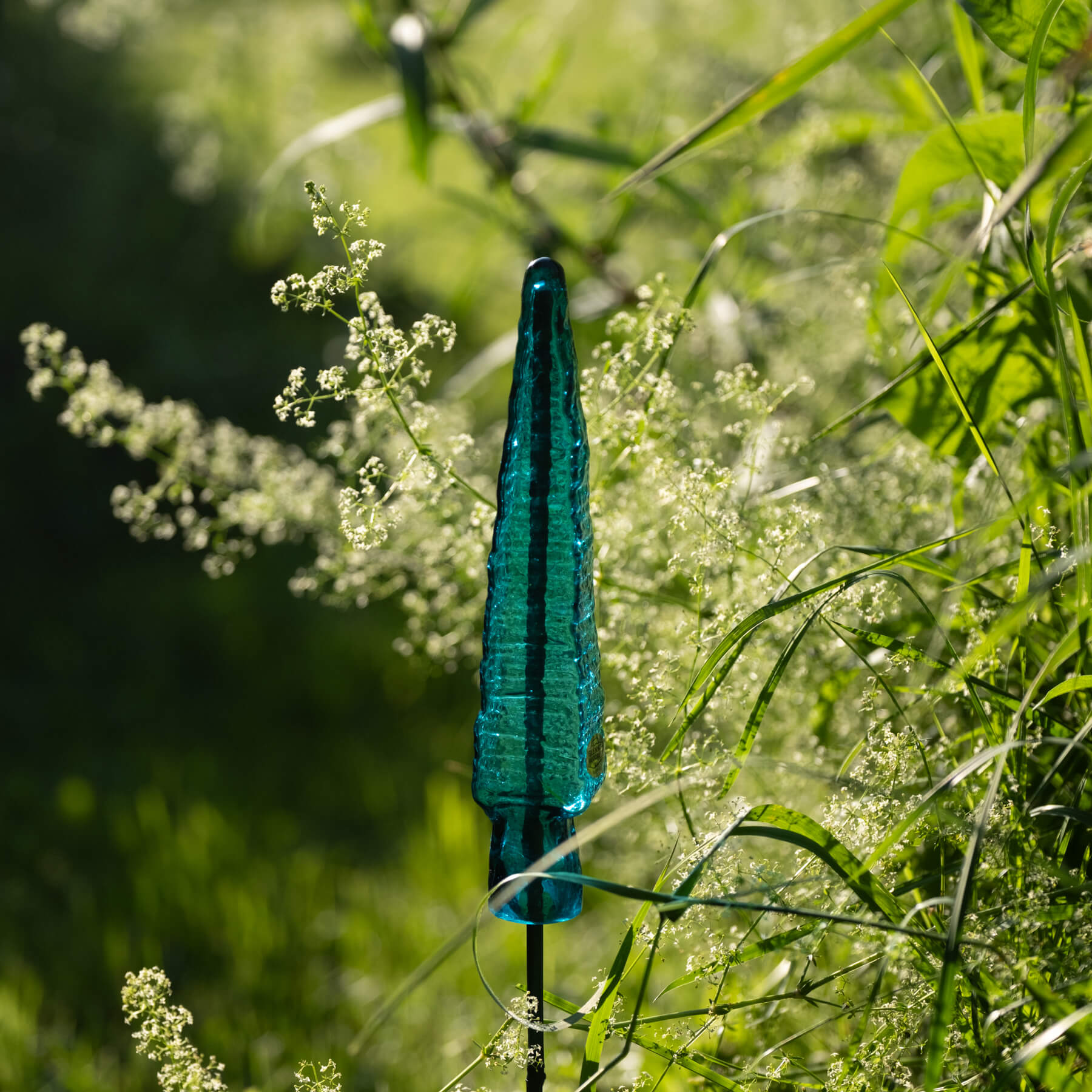 Blue glass garden stake among green plants