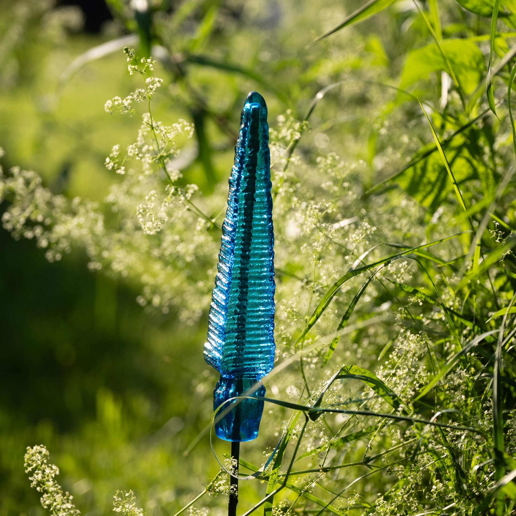 Blue glass sculpture among green grass and plants