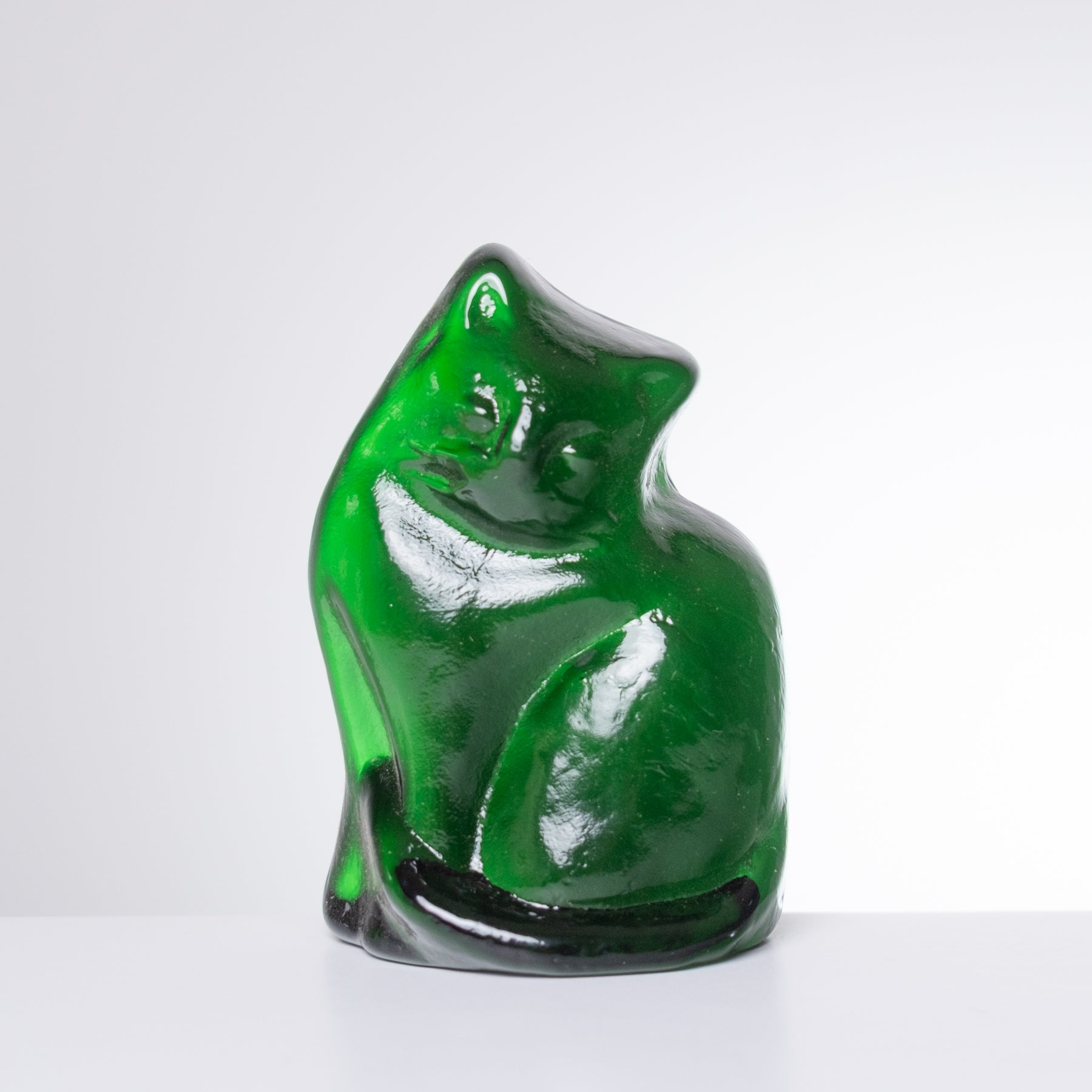 A glossy green glass figurine of a sitting cat, displayed on a clean white surface against a light gray background.