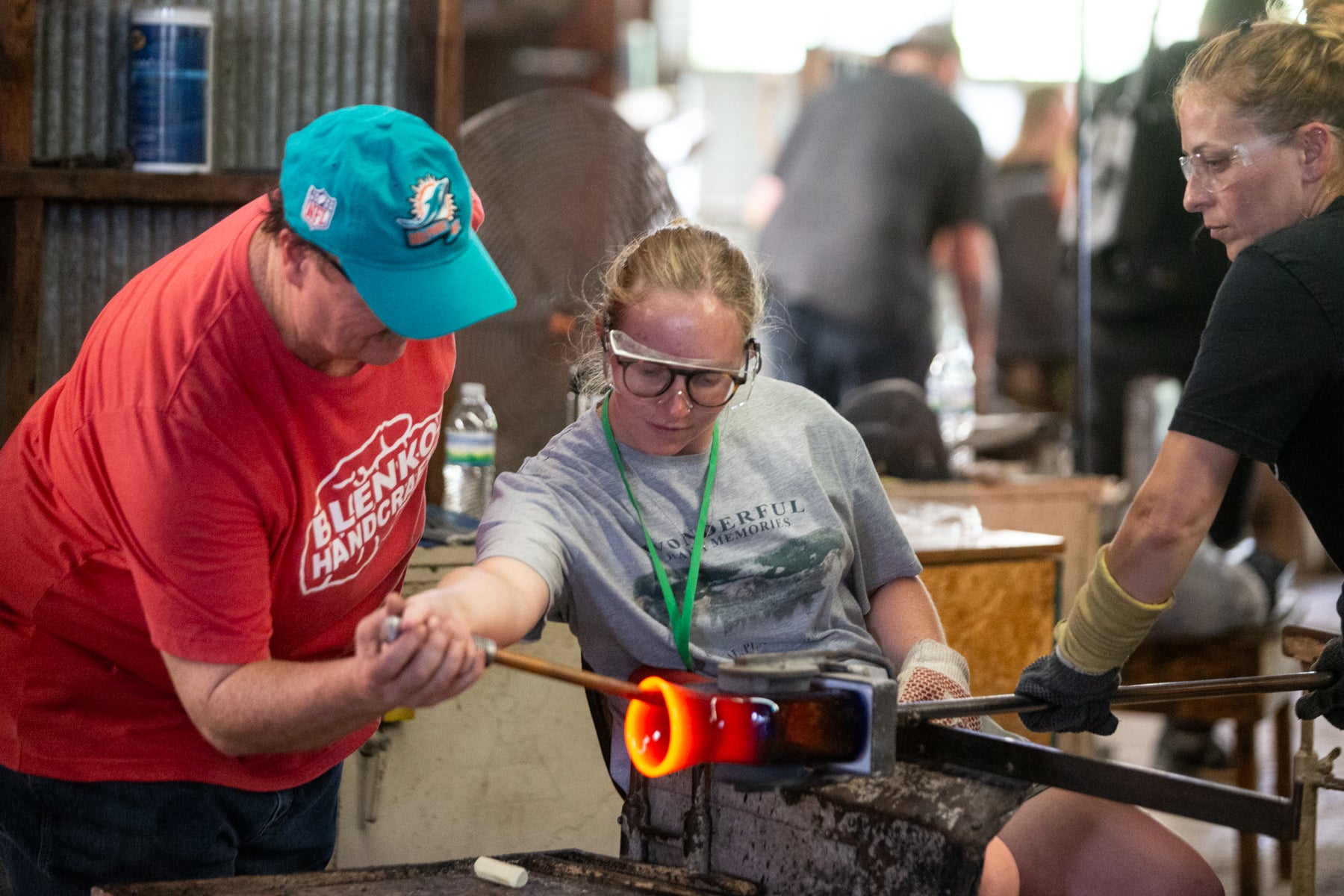 Two people working with glassblowing tools in a workshop setting.