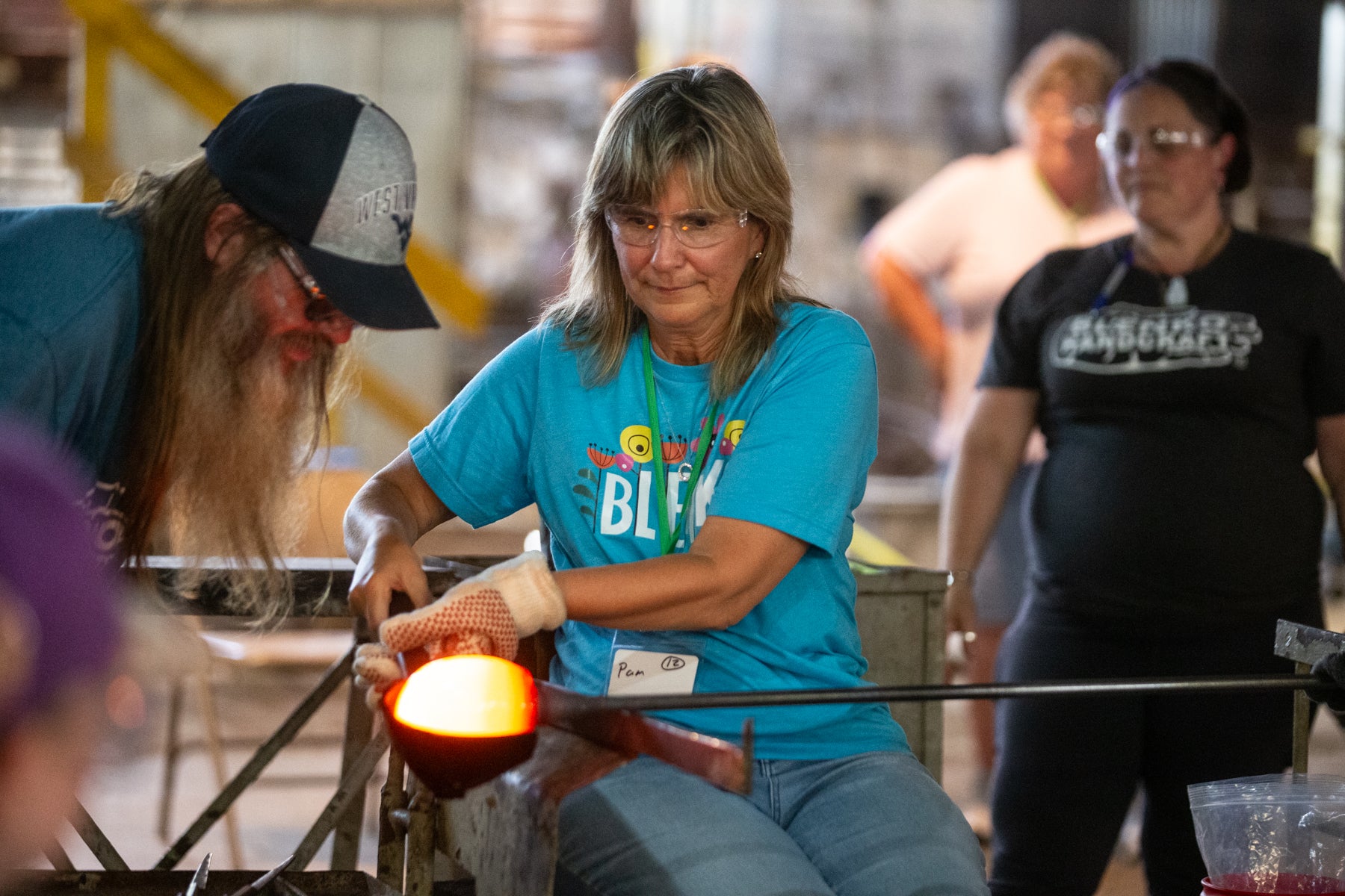 Person working with glass in a workshop setting with other people around
