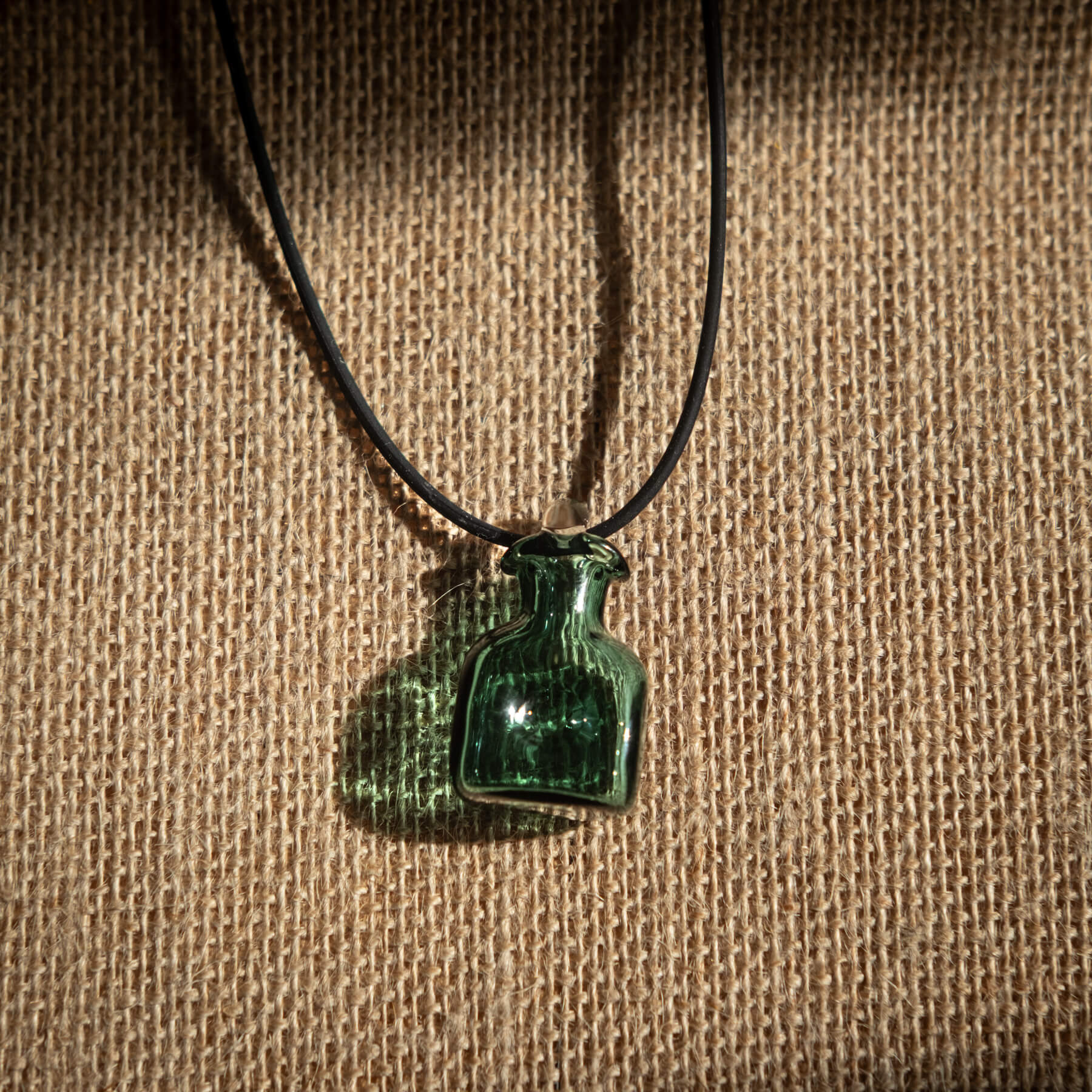 Green glass bottle pendant on a black cord against a brown fabric background