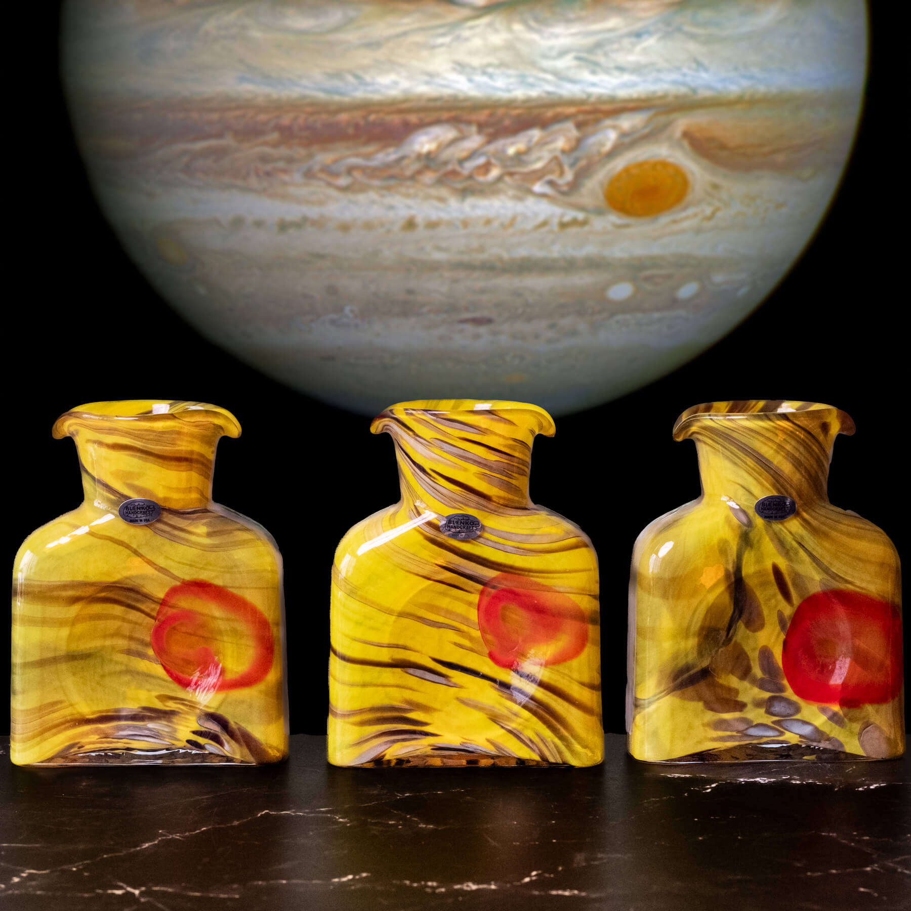 Three glass bottles with a red circle design in front of a large image of Jupiter.