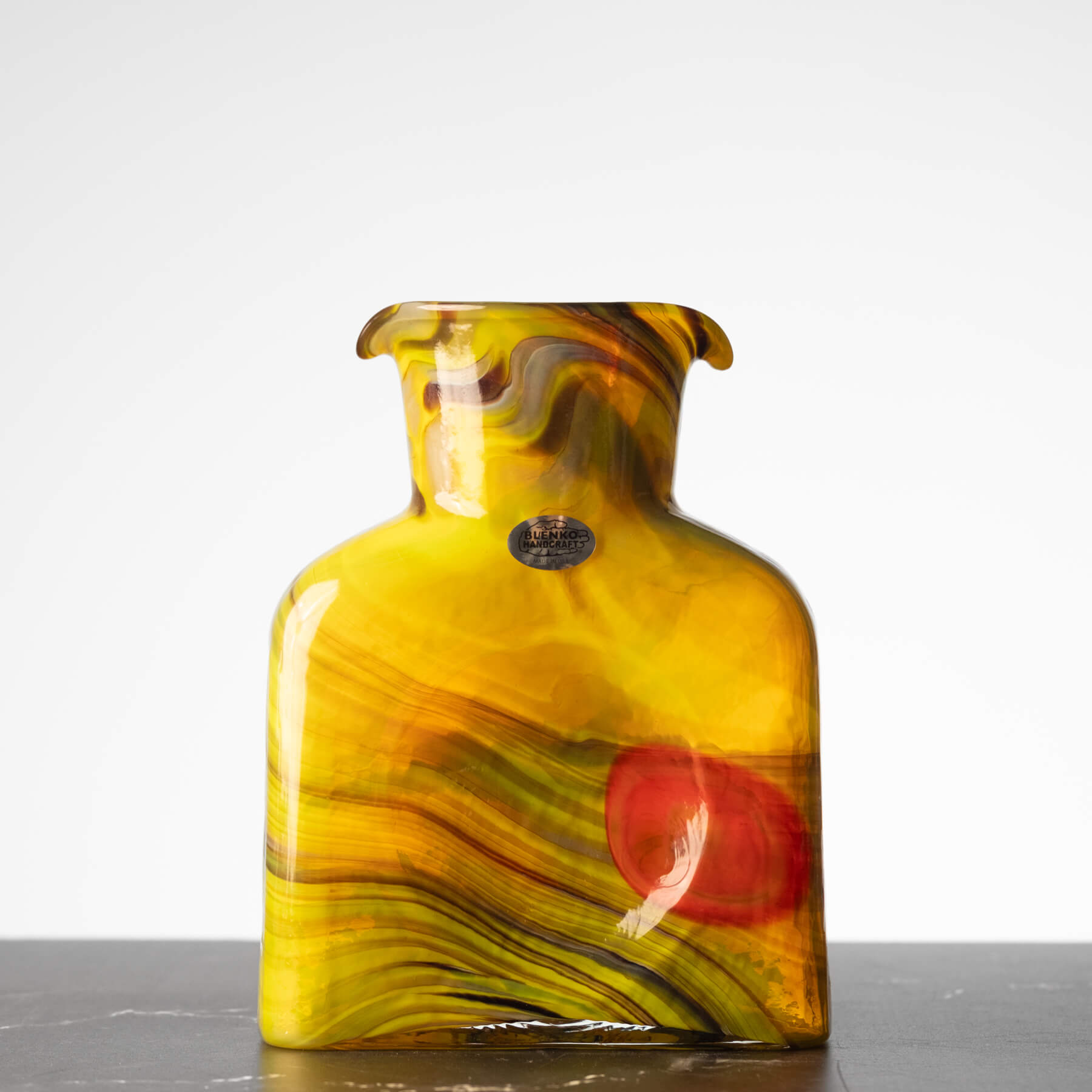 Glass vase with yellow and red swirl pattern on a white background