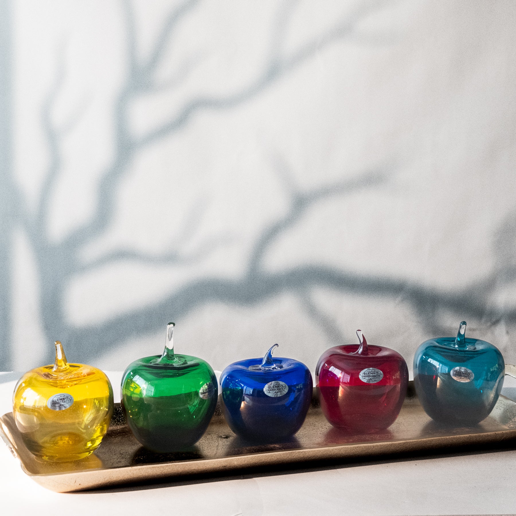 Five colorful glass apples on a tray with a neutral background