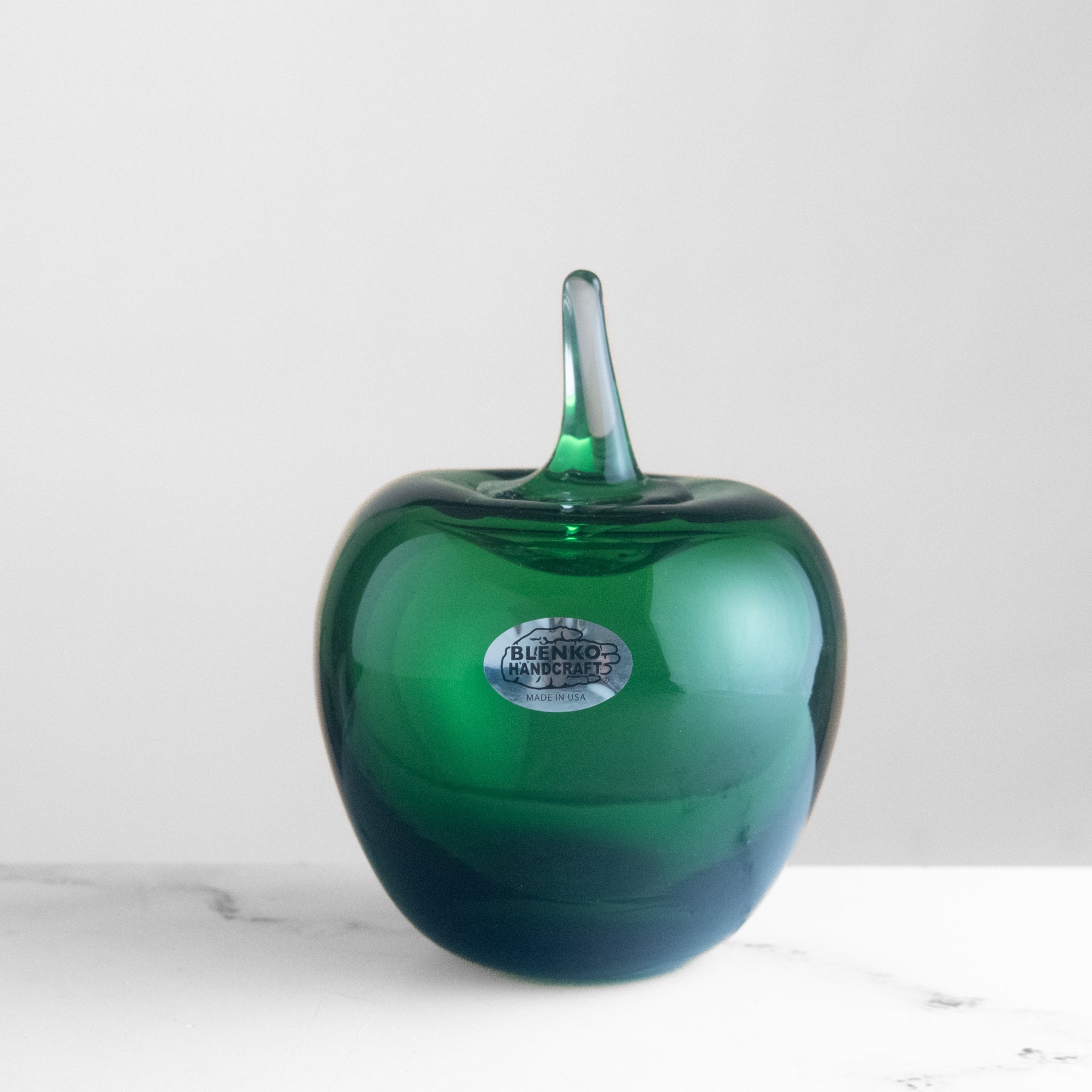 Green glass apple-shaped object with a stem on a white background