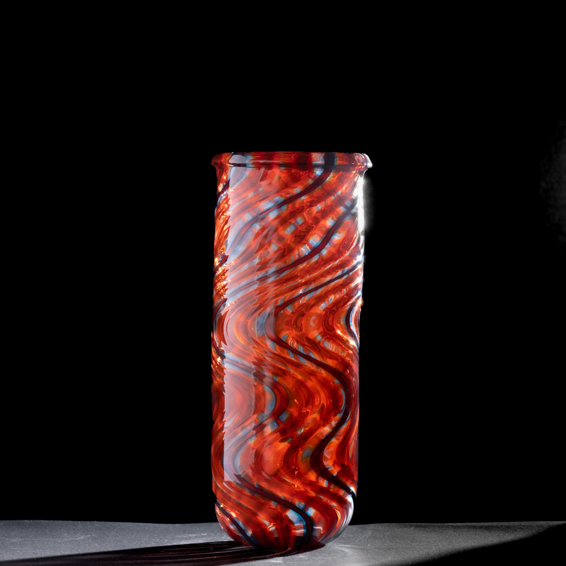 Tall cylindrical glass vase with red and blue swirl pattern on a black background