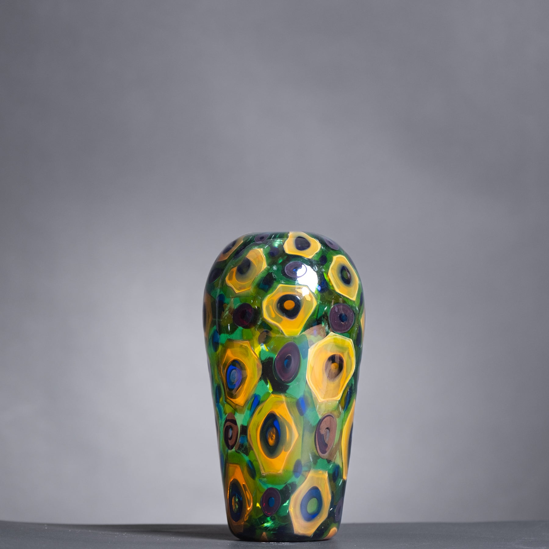 Decorative glass vase with colorful circular patterns on a gray background