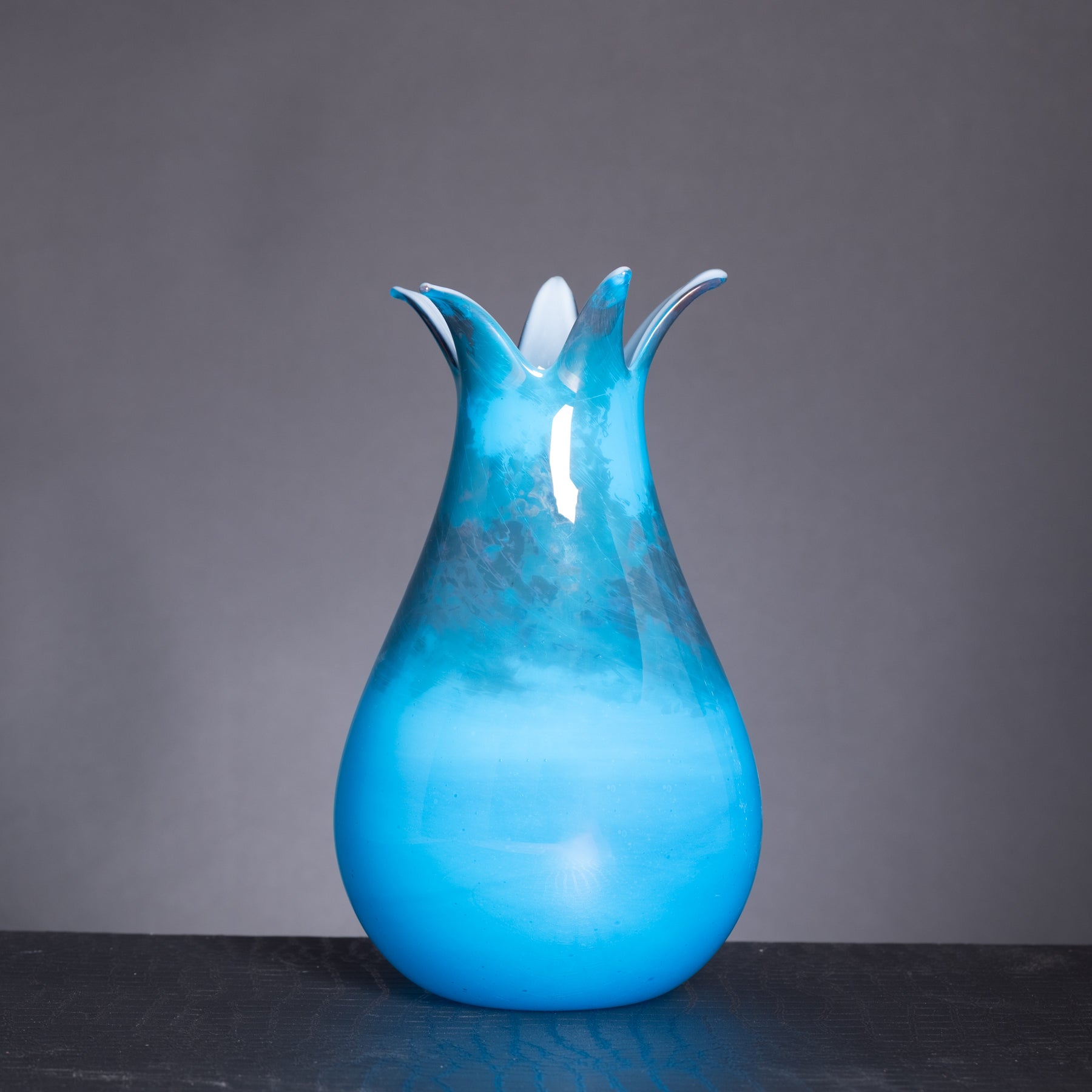 Blue glass vase with a unique design on a dark surface and gray background