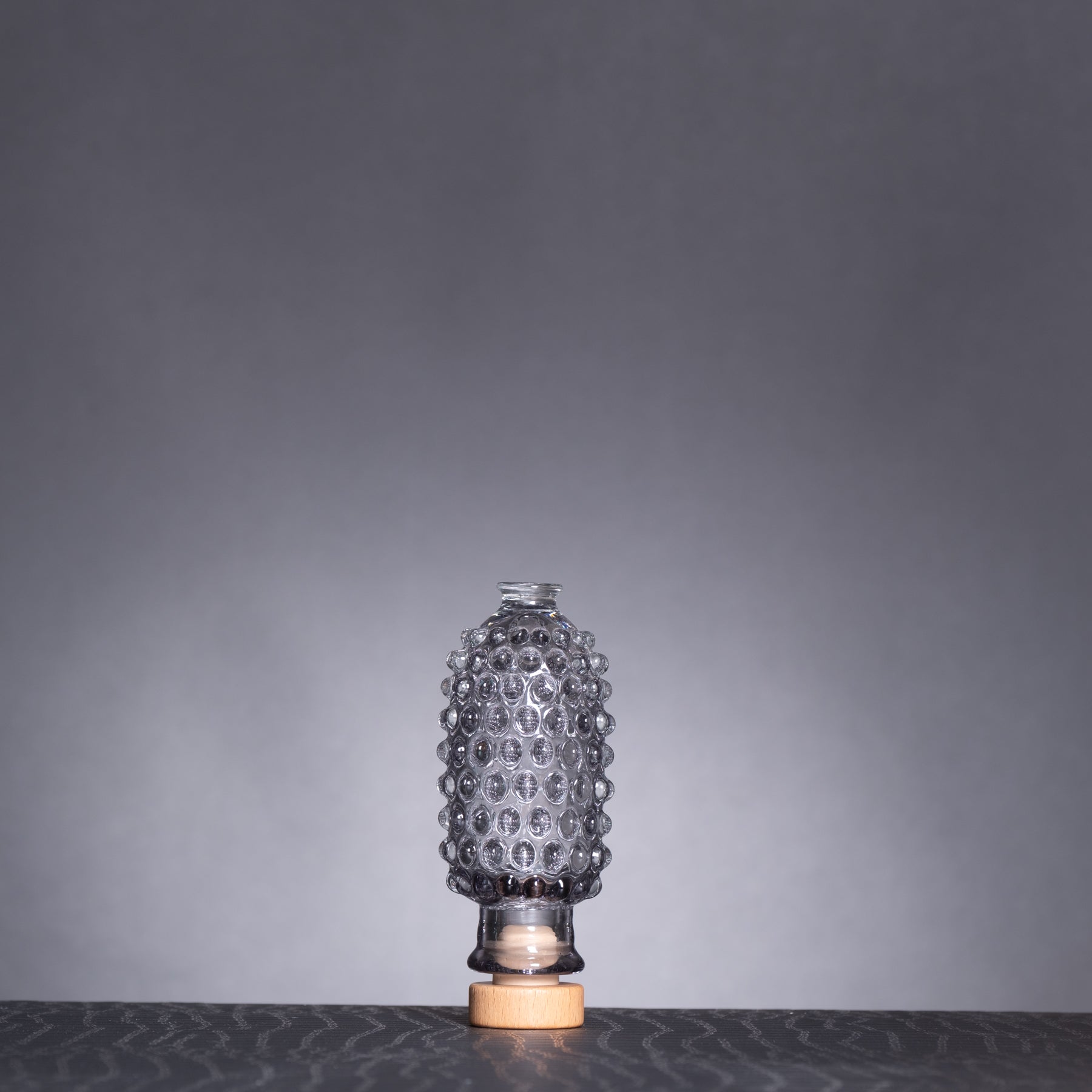 Decorative glass bottle with textured design on a dark surface and gray background