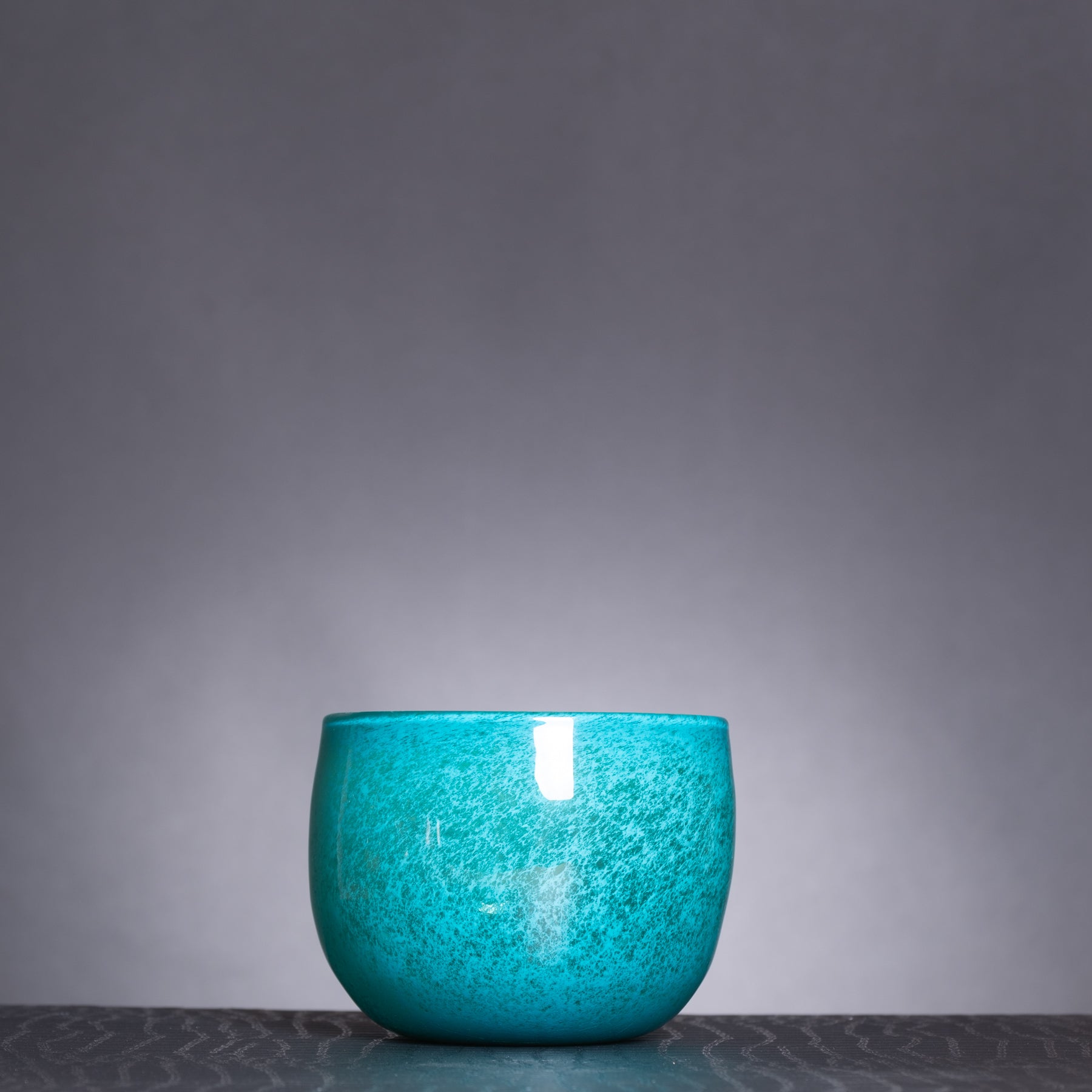 Turquoise glass bowl on a dark surface with a gray background