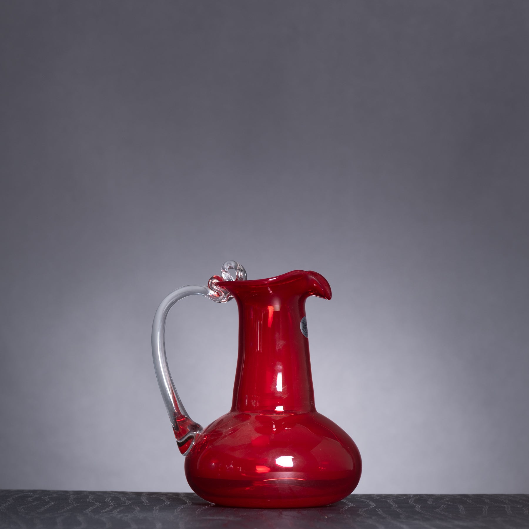 Red glass pitcher on a dark surface with a gray background