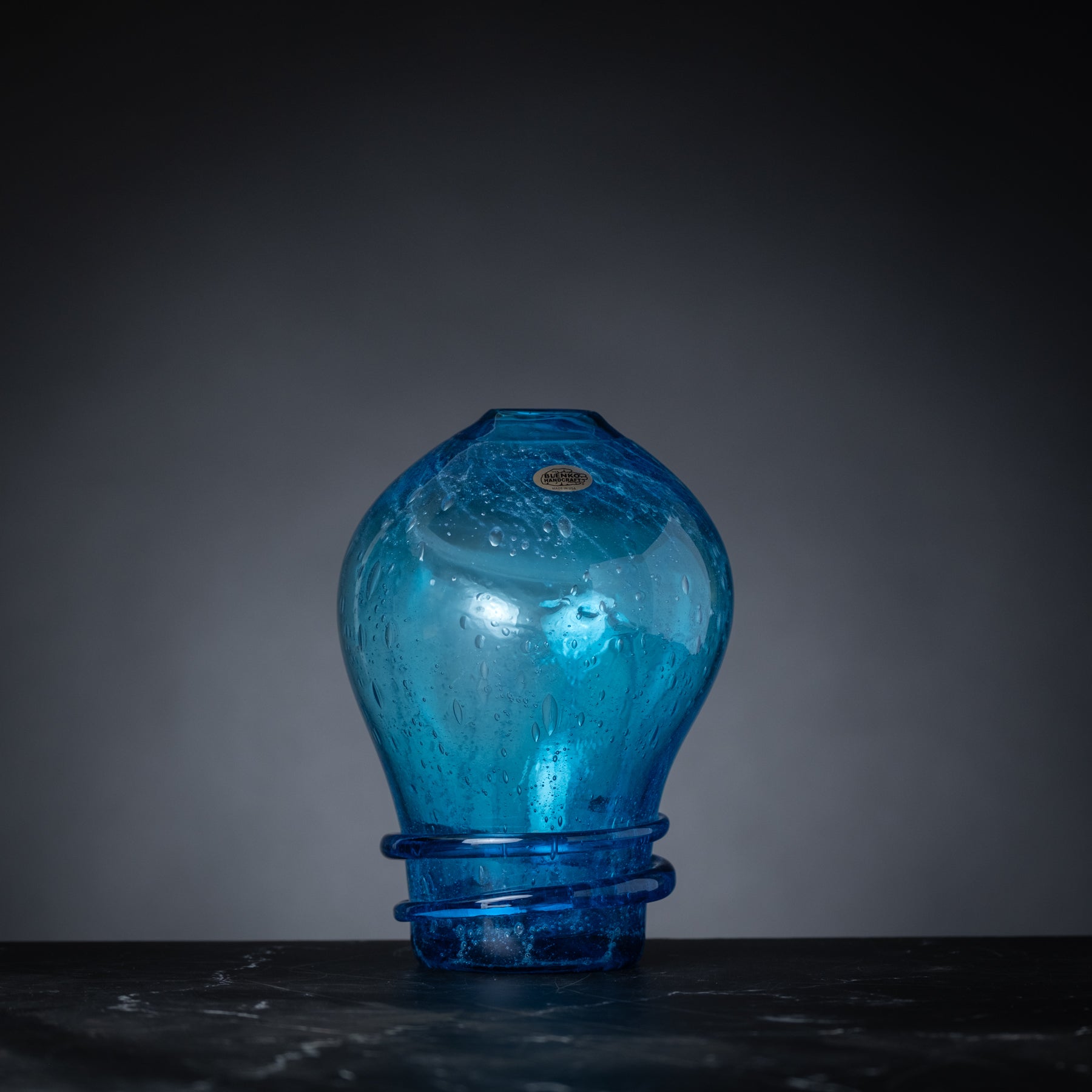 Blue glass light bulb-shaped vase on a dark surface with a gray background