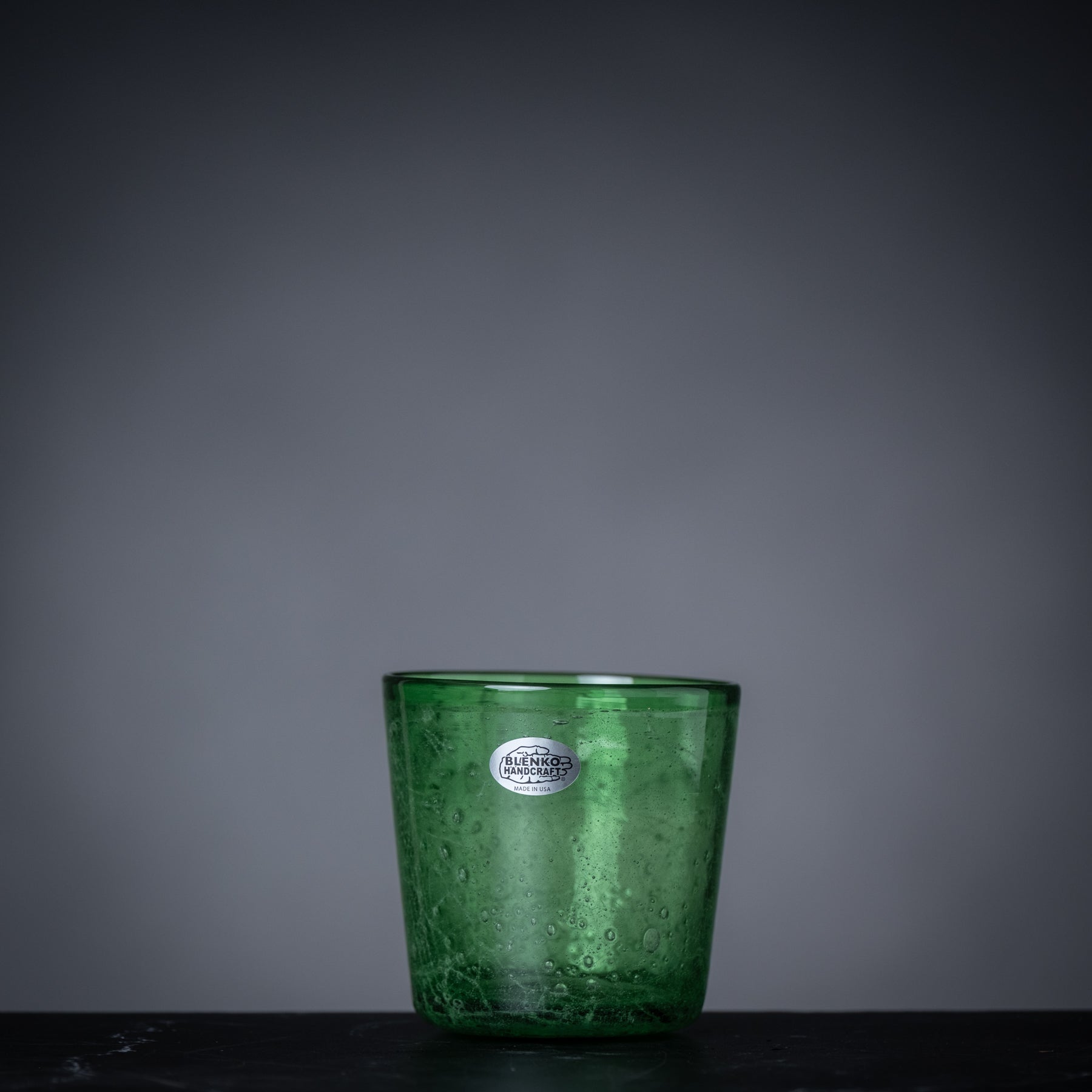 Green glass candle holder with a label on a dark surface and gray background