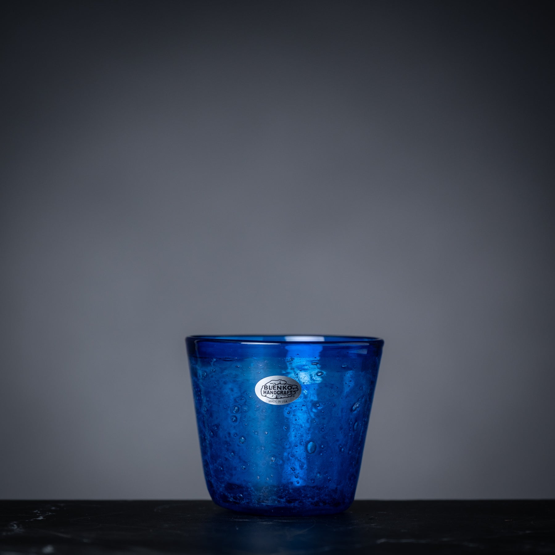 Blue glass cup with a logo on a dark surface and gray background
