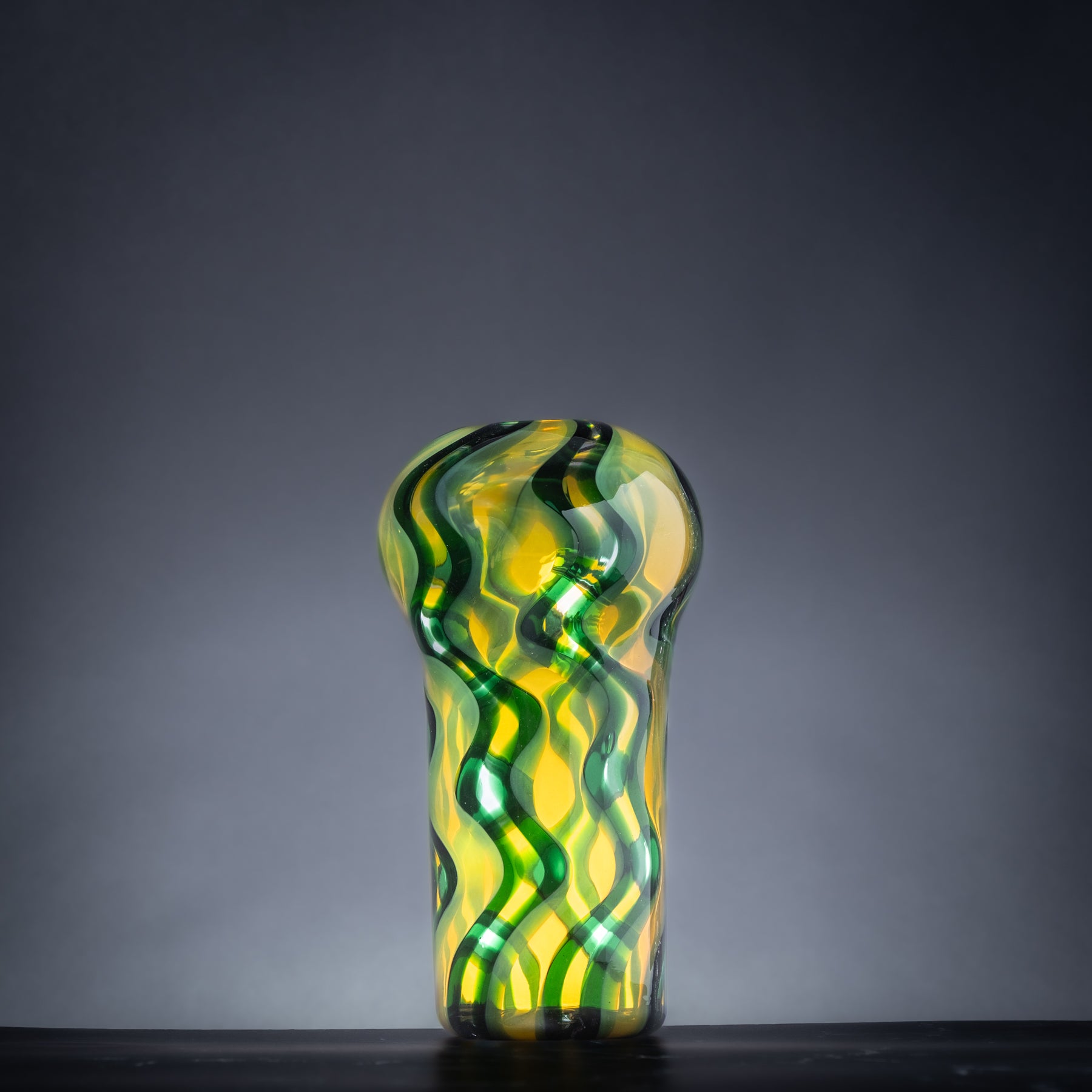 Glass vase with green and yellow wavy pattern on a dark background