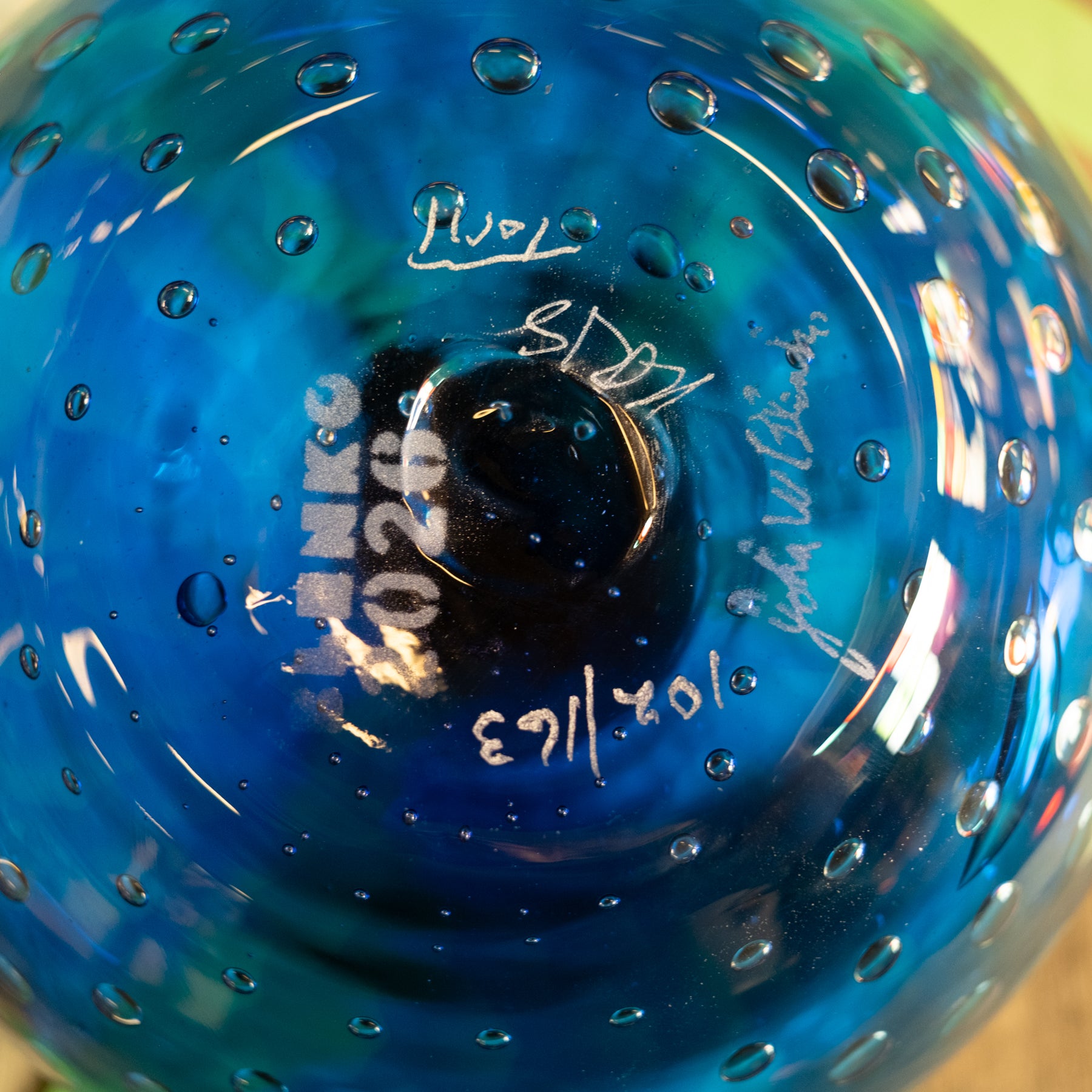 Close-up of the bottom of a blue glass bowl with a textured bubble pattern and white handwritten markings.
