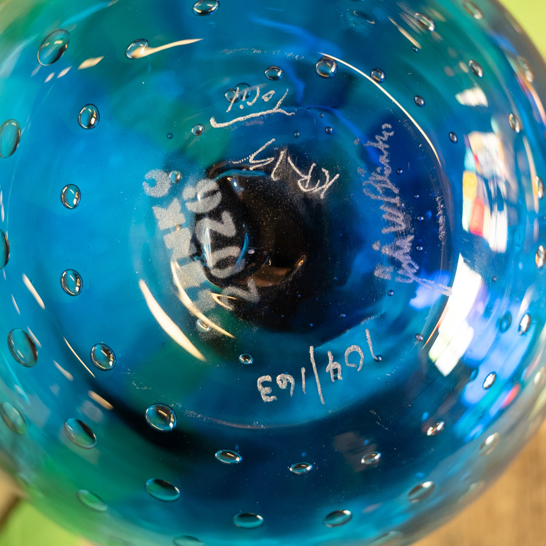 Close-up of a blue and teal glass bowl with a textured bubble pattern and white hand-written markings on the bottom.