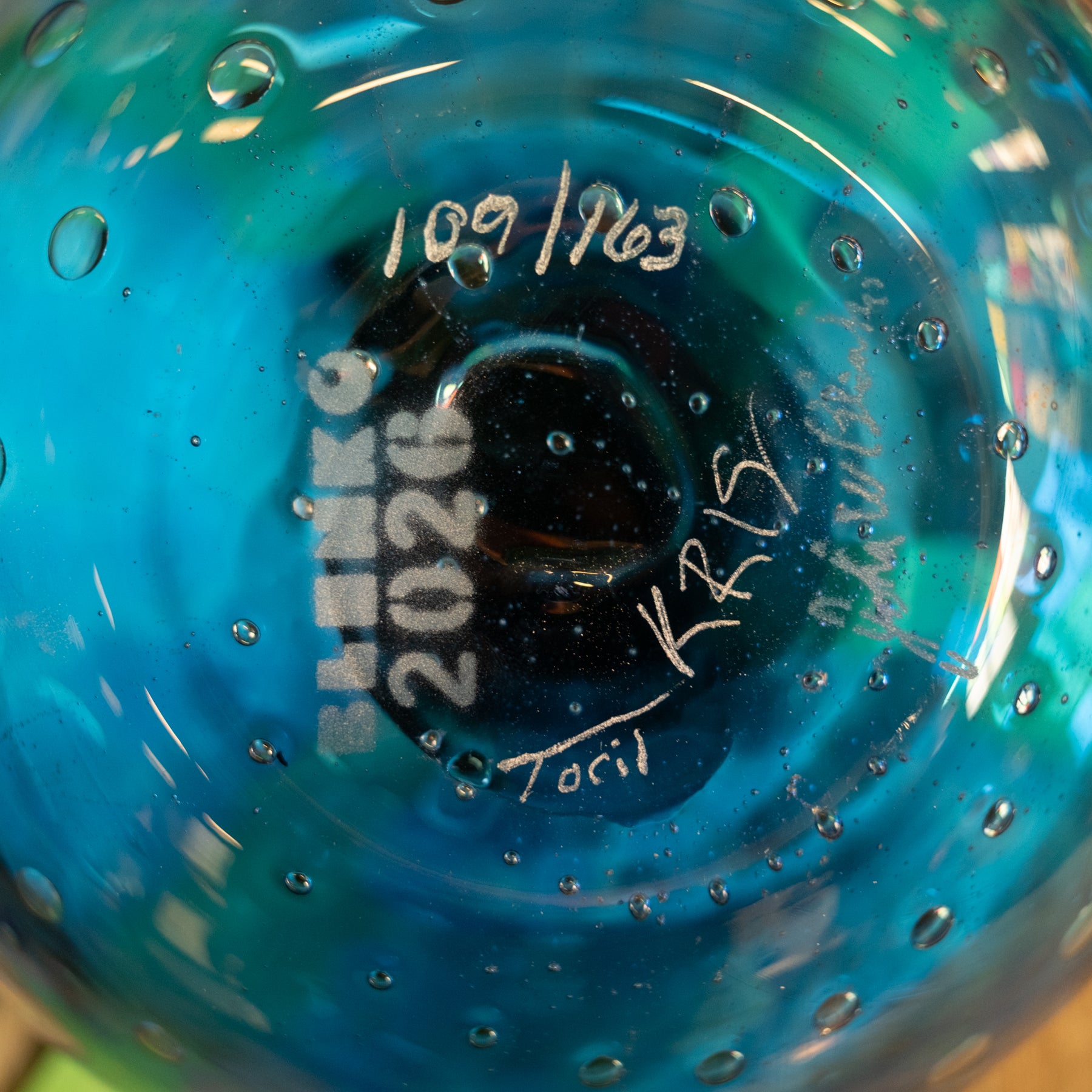 Close-up of the bottom of a blue glass bottle or vase with handwritten white markings, including the date 10.09.