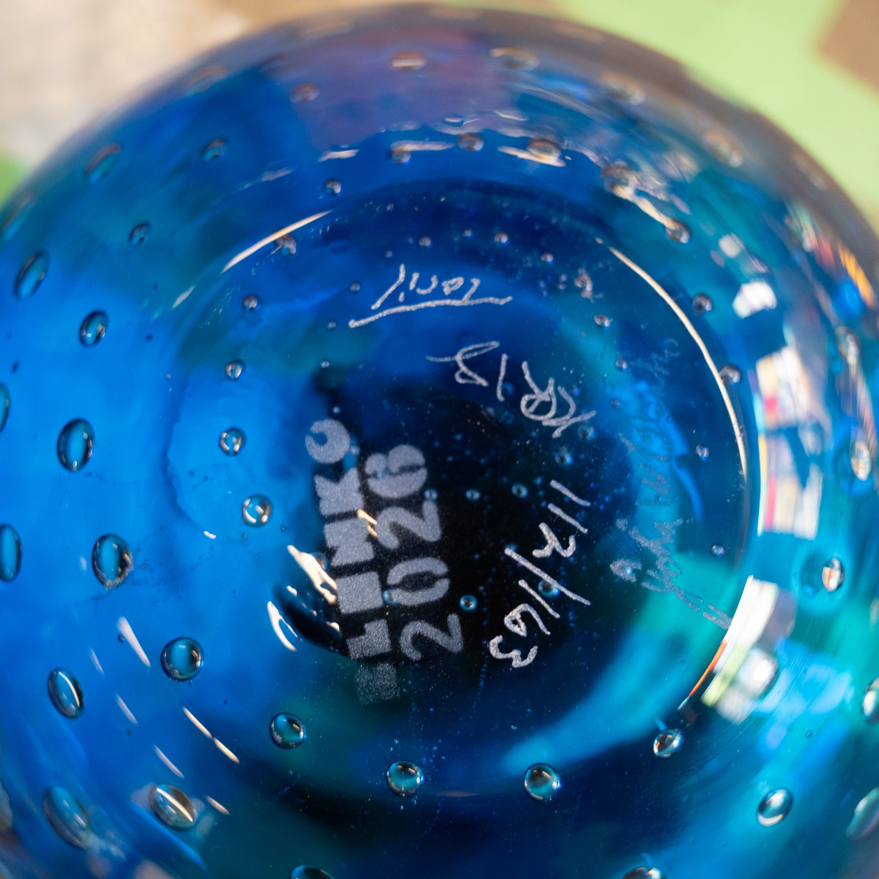 Close-up of the bottom of a transparent blue glass bowl or vase with a bubbled texture and white handwritten markings.