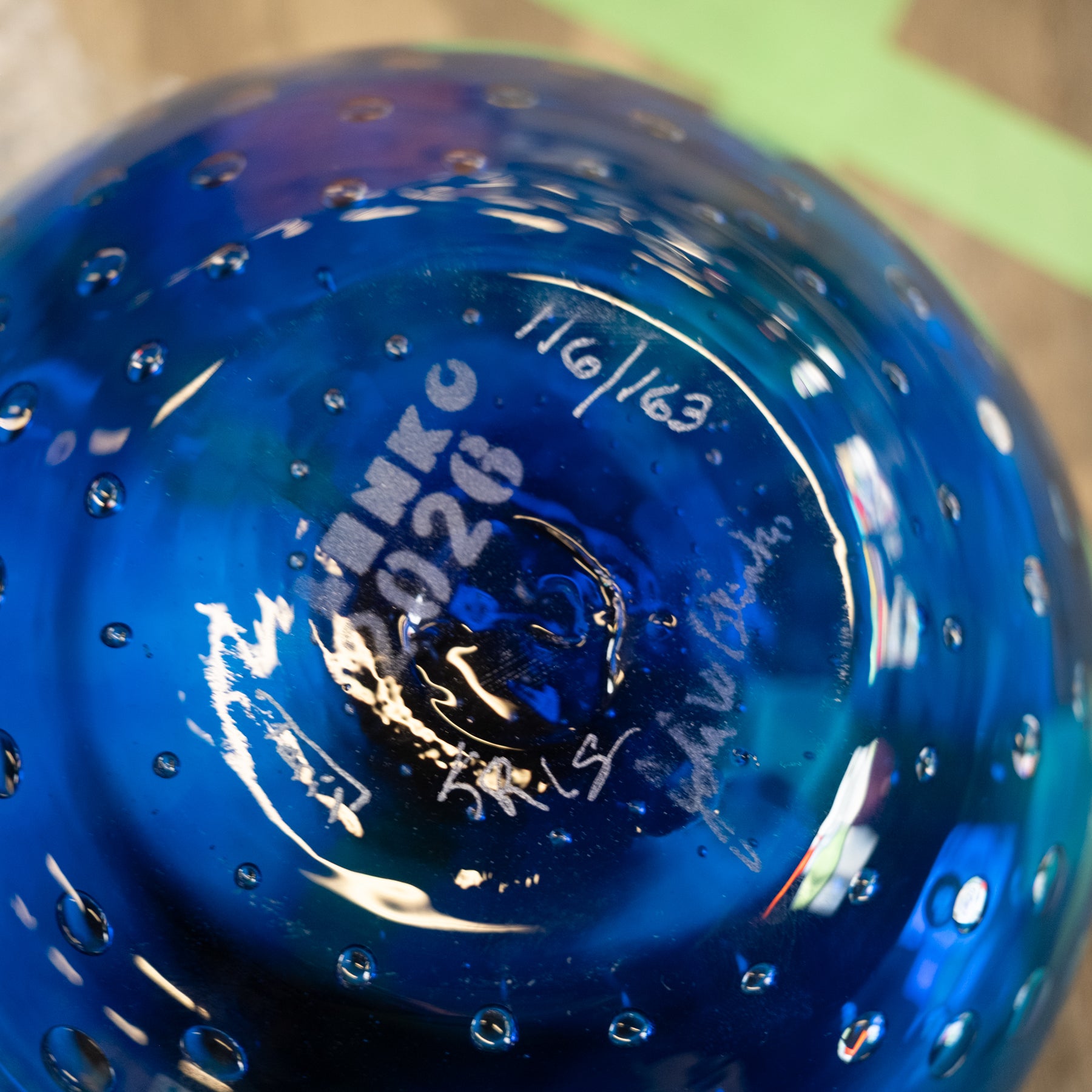Close-up of the bottom of a blue glass bowl with bubble texture and white etched markings including the brand name 'MINKO' and date '11/01/63'.