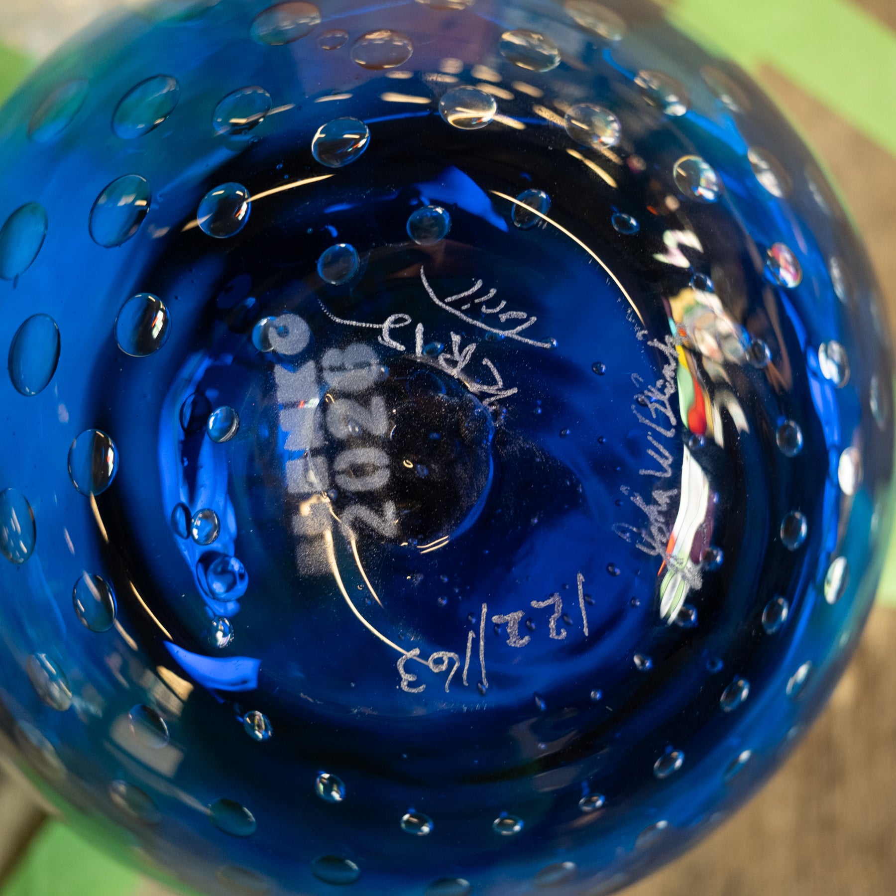 Close-up of the bottom of a transparent cobalt blue glass bowl with a bubble pattern and white hand-written markings.