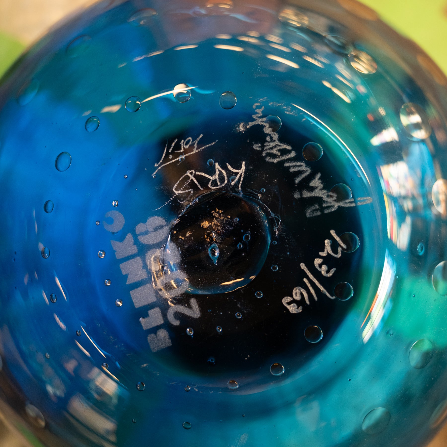 Close-up of the bottom of a transparent blue glass bowl or vase with handwritten white markings and bubble details.