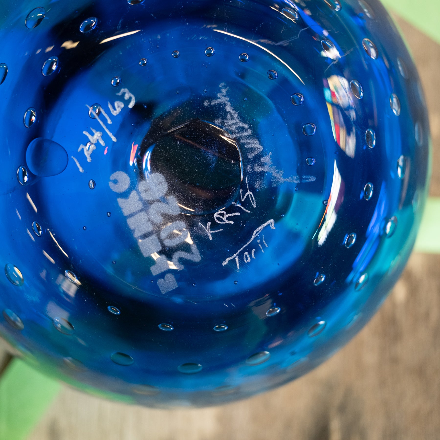 Close-up of the bottom of a translucent cobalt blue glass bowl or vase with a bubble pattern and white handwritten markings.