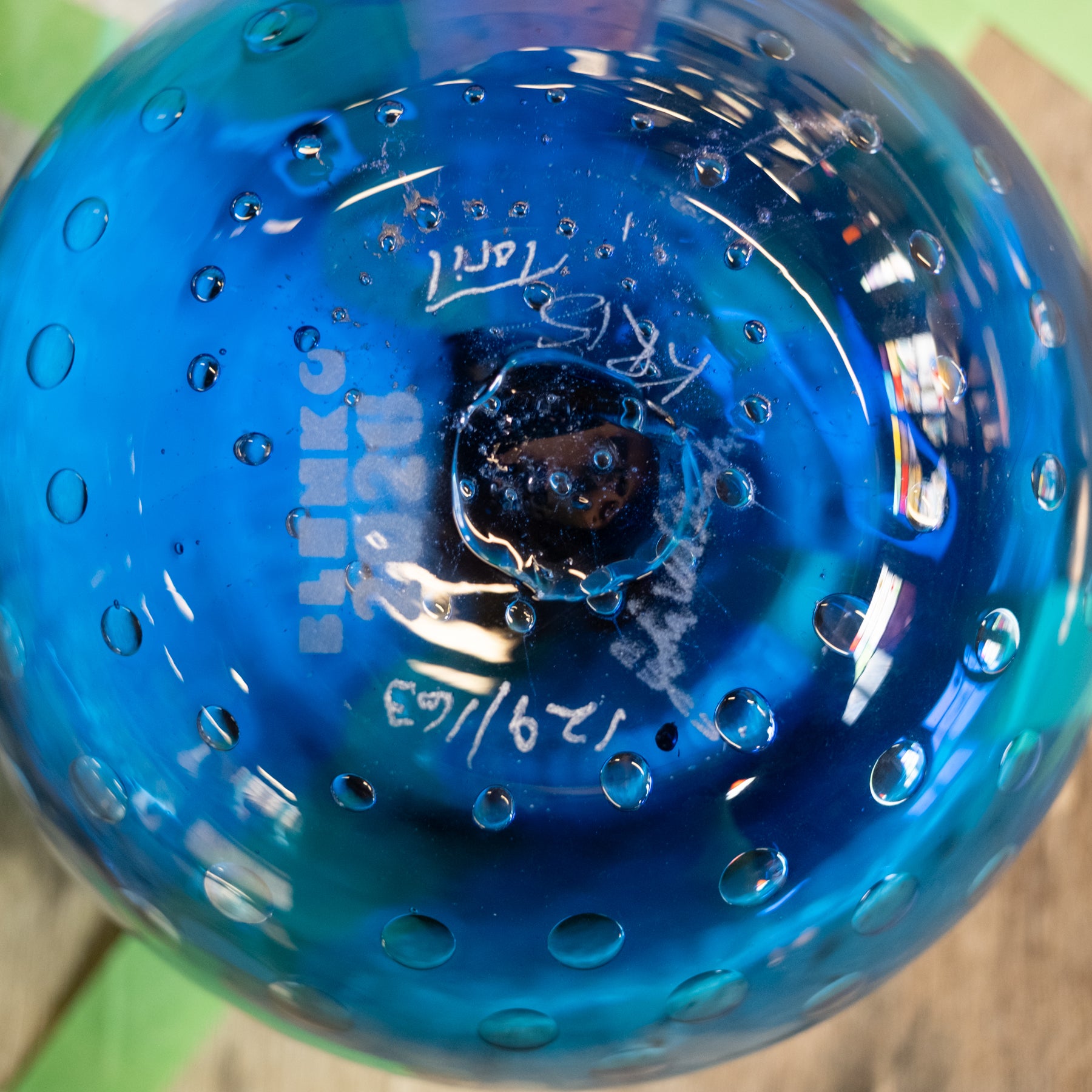 A close-up of a blue glass bowl with a textured bubble pattern and white hand-written markings on the bottom.