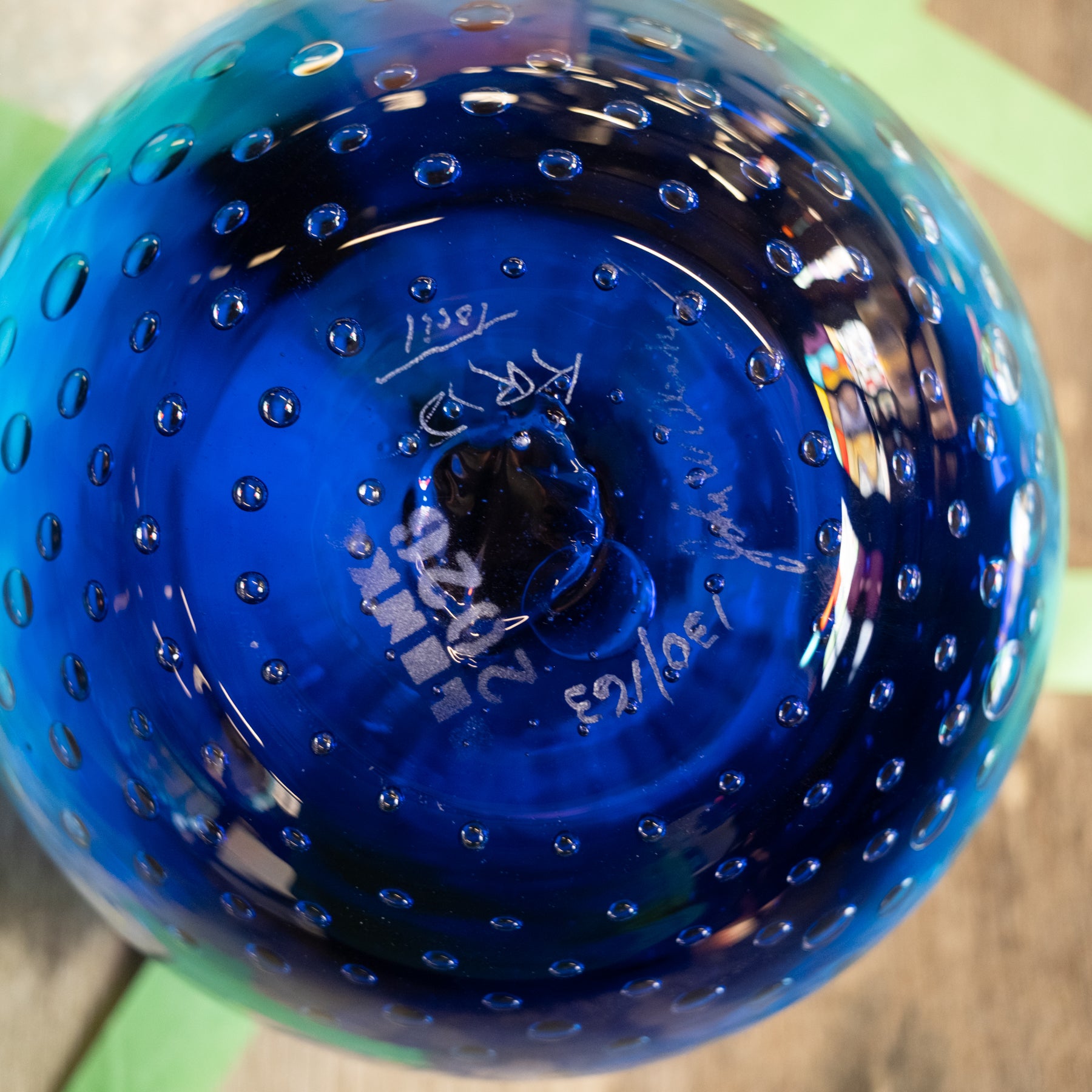 A close-up of a cobalt blue glass vase with a textured bubble pattern and handwritten markings on the bottom.