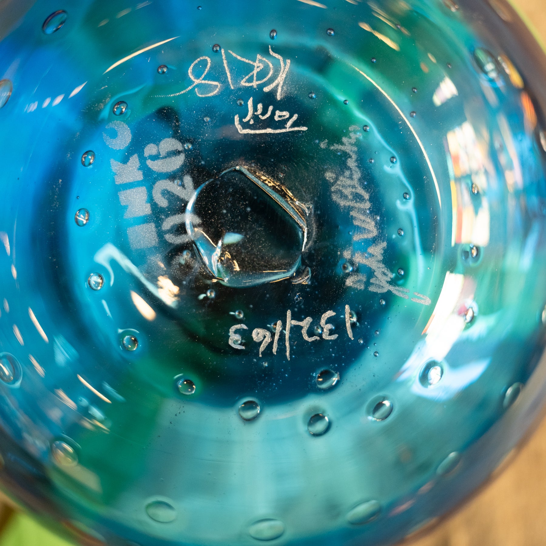 Close-up of the bottom of a transparent blue glass bowl or vase with white handwritten markings and bubble details.