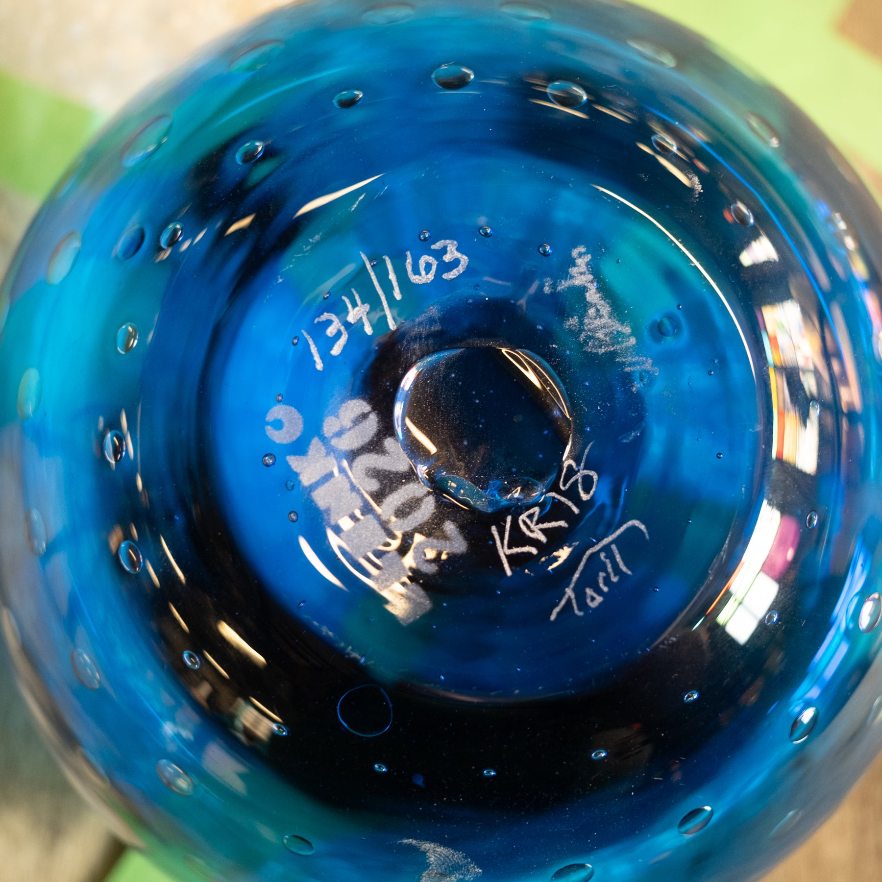 Close-up of the bottom of a translucent blue glass vessel with white handwritten markings and small bubble details around the rim.