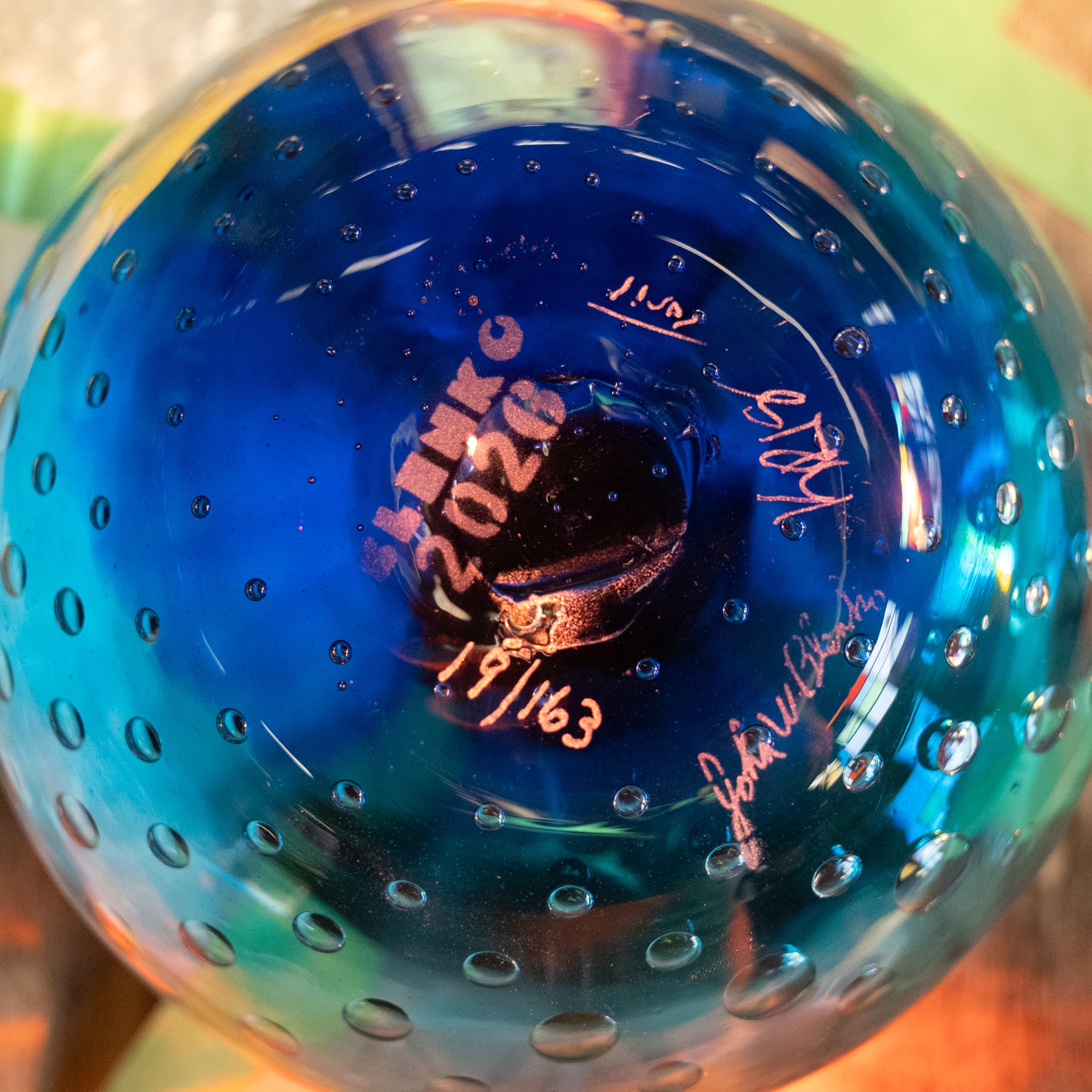 Close-up of a blue glass bowl with a bubble pattern and handwritten markings inside the base.