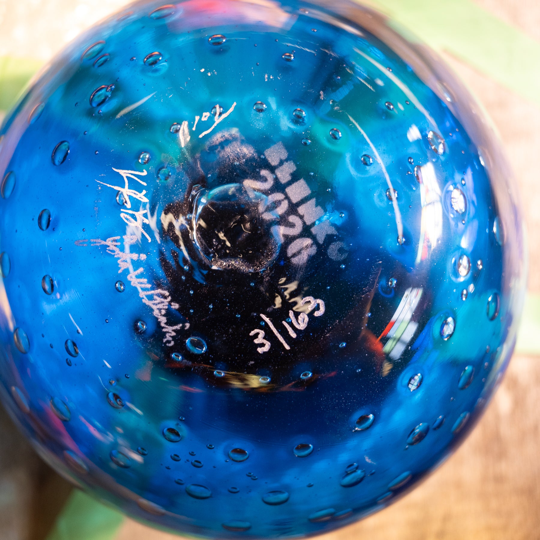 A close-up of a blue glass decorative object, likely a vase or bowl, featuring a bubbled texture and white handwritten markings on the bottom.