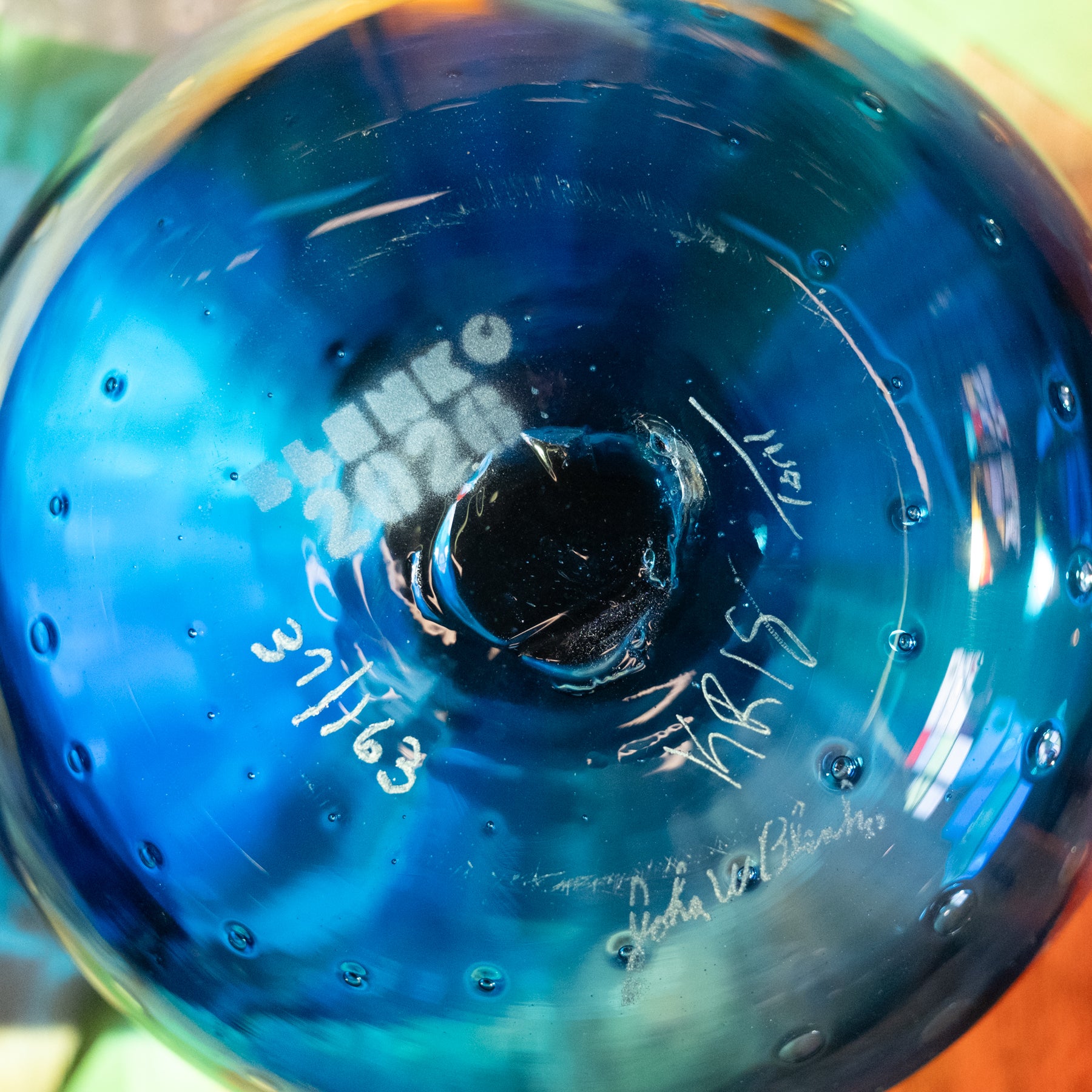 Close-up of a blue glass bottle or vase with a circular opening, showing white printed text and signatures on the inside surface.
