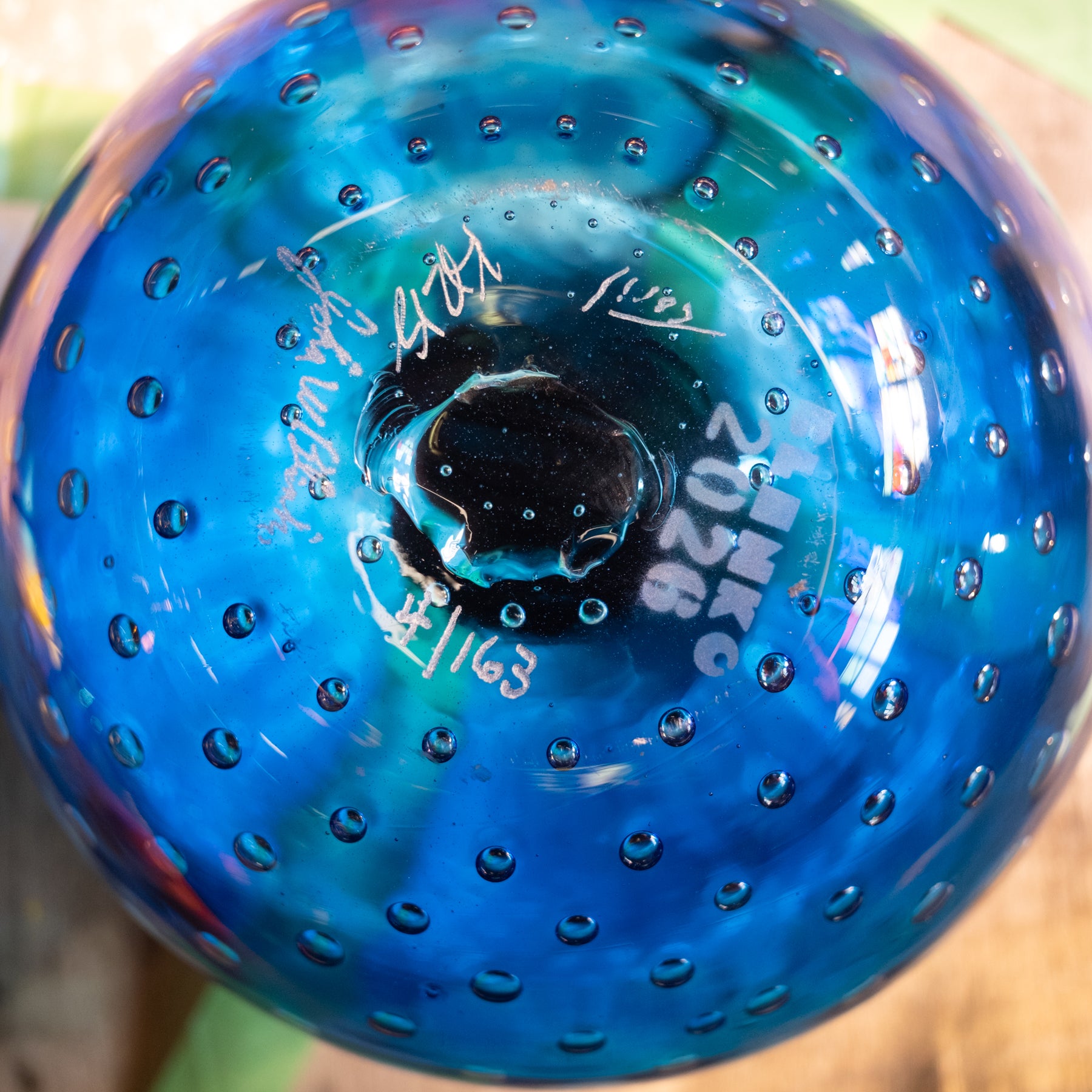 A close-up of a blue glass bowl with a textured bubble pattern and white hand-written markings on the bottom.