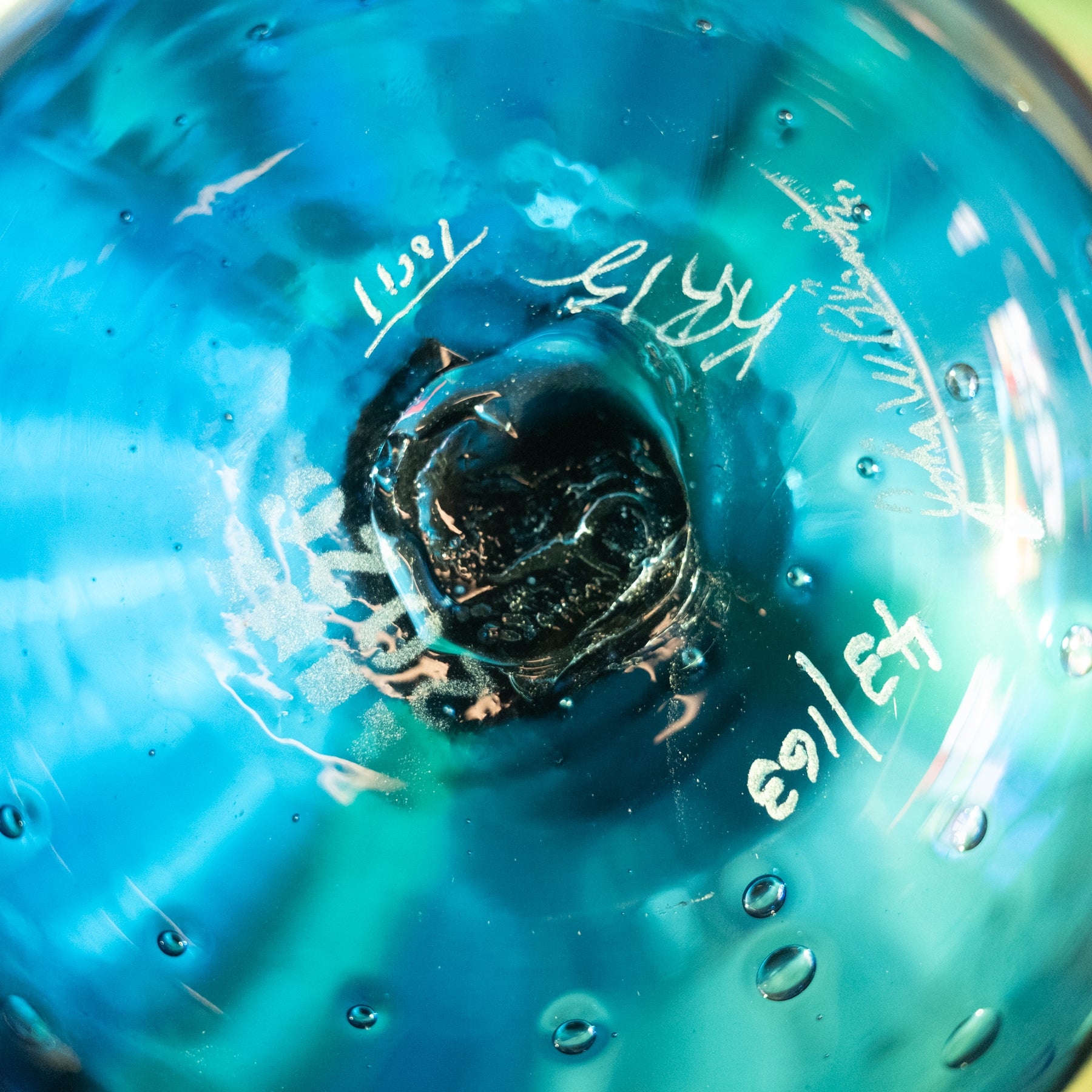 Close-up of a blue glass vessel viewed from inside, showing a dark central opening and white handwritten markings on the glass surface.