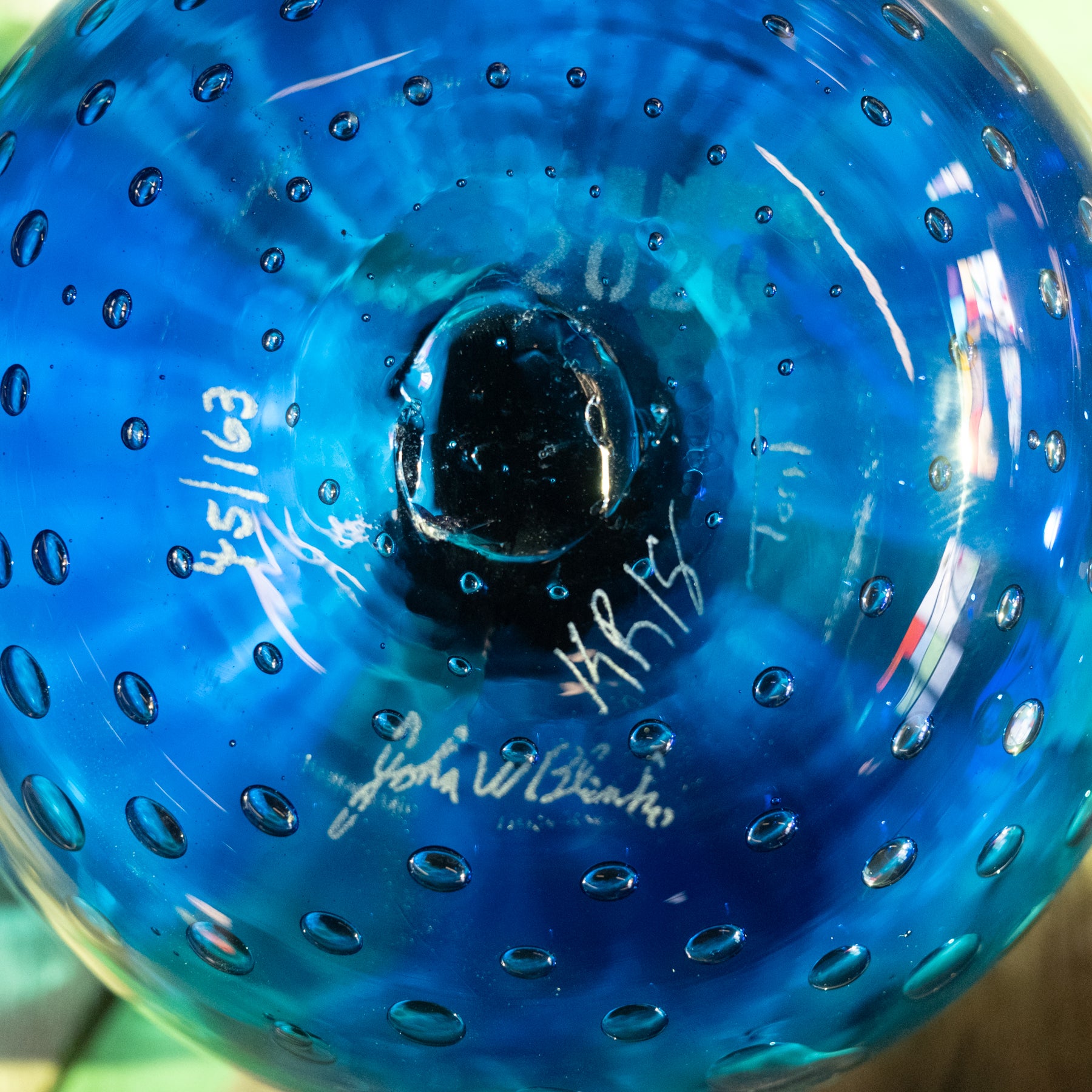 A close-up of a blue glass bowl with a textured, dimpled surface and white printed signatures on the inside.