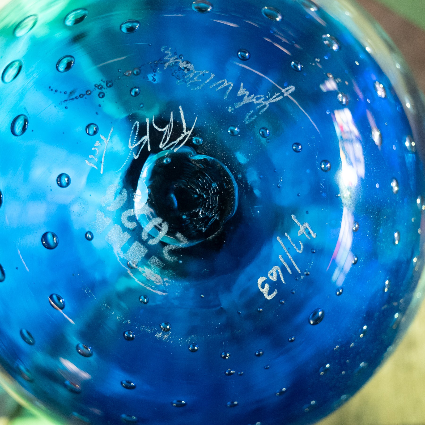 A close-up of a blue glass bowl with a textured, bubbly surface and white handwritten markings.