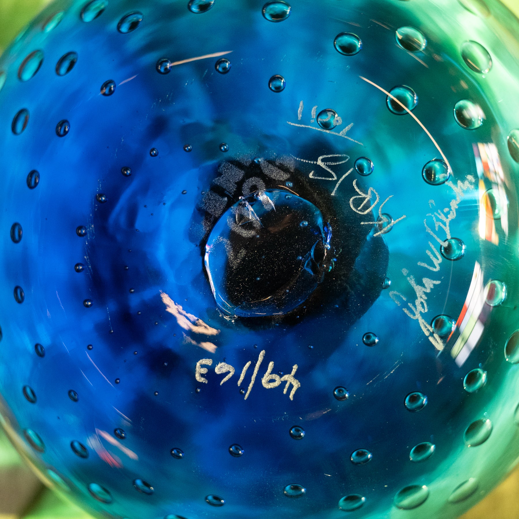 Close-up of a blue and green glass bowl with a textured bubble pattern and white handwritten markings inside the rim.