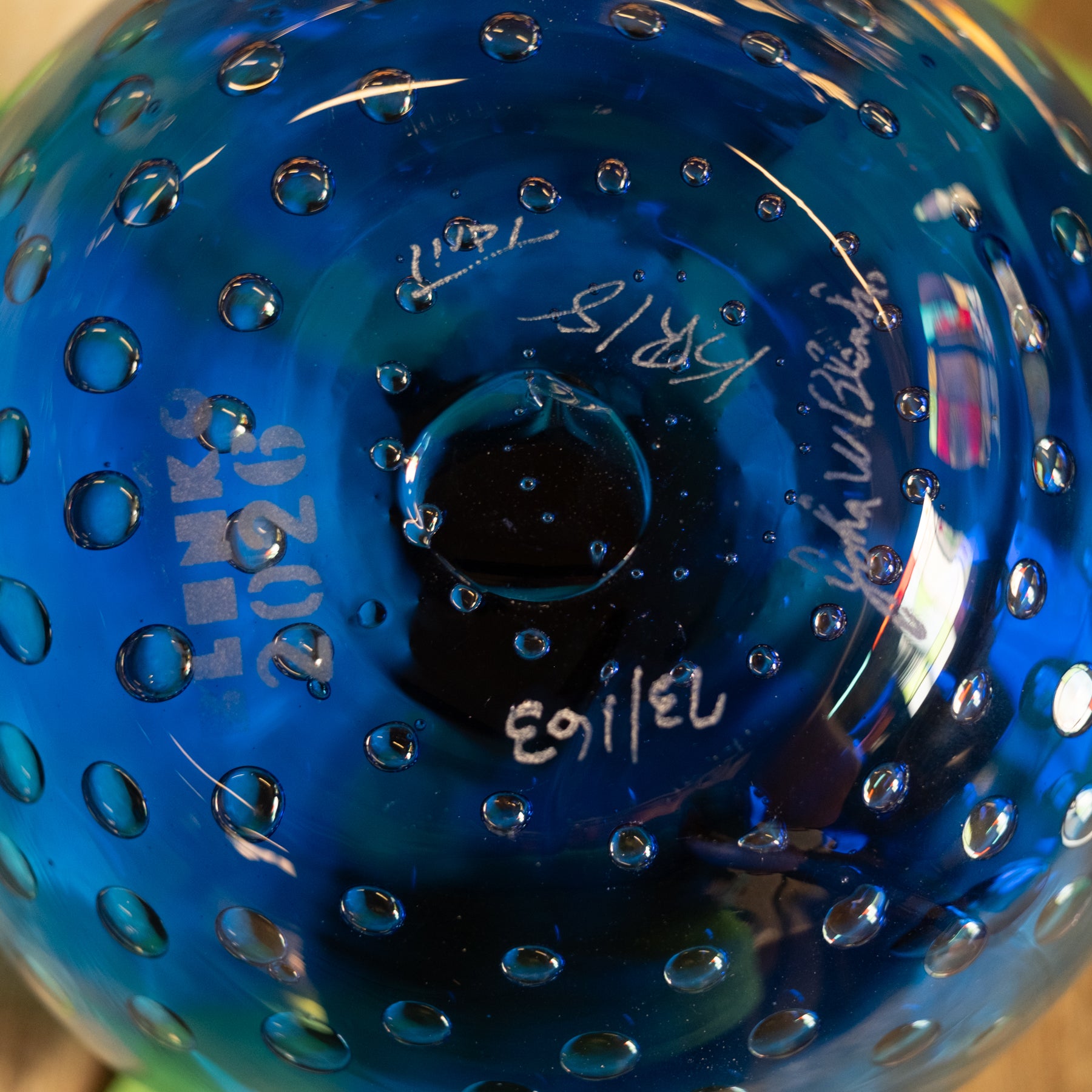 Close-up of the bottom of a transparent blue glass bowl with a bubble pattern and white handwritten markings.