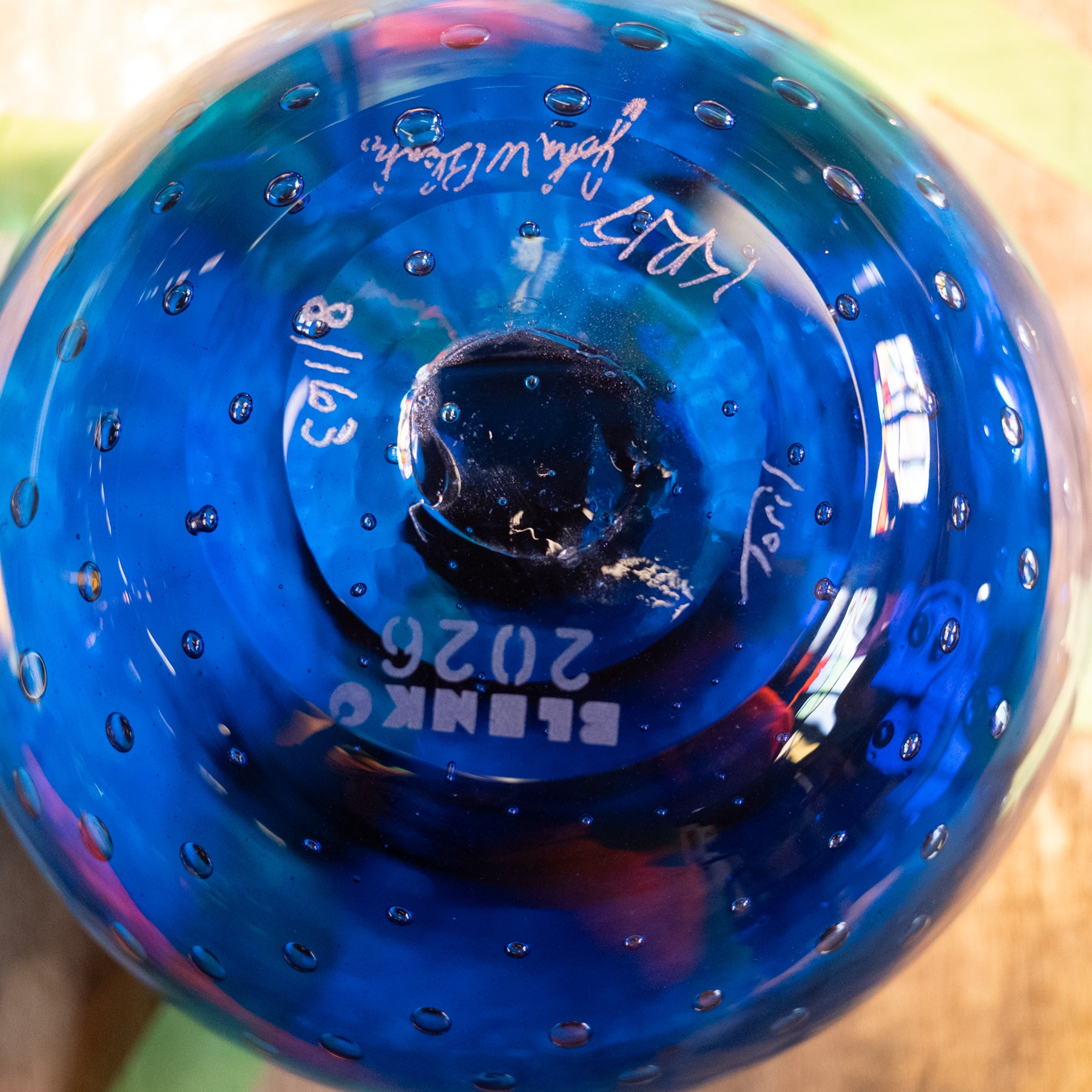 A close-up of a blue glass orb with a textured, bubbled surface and white printed text reading 'ELLENKO 2026' on the bottom.